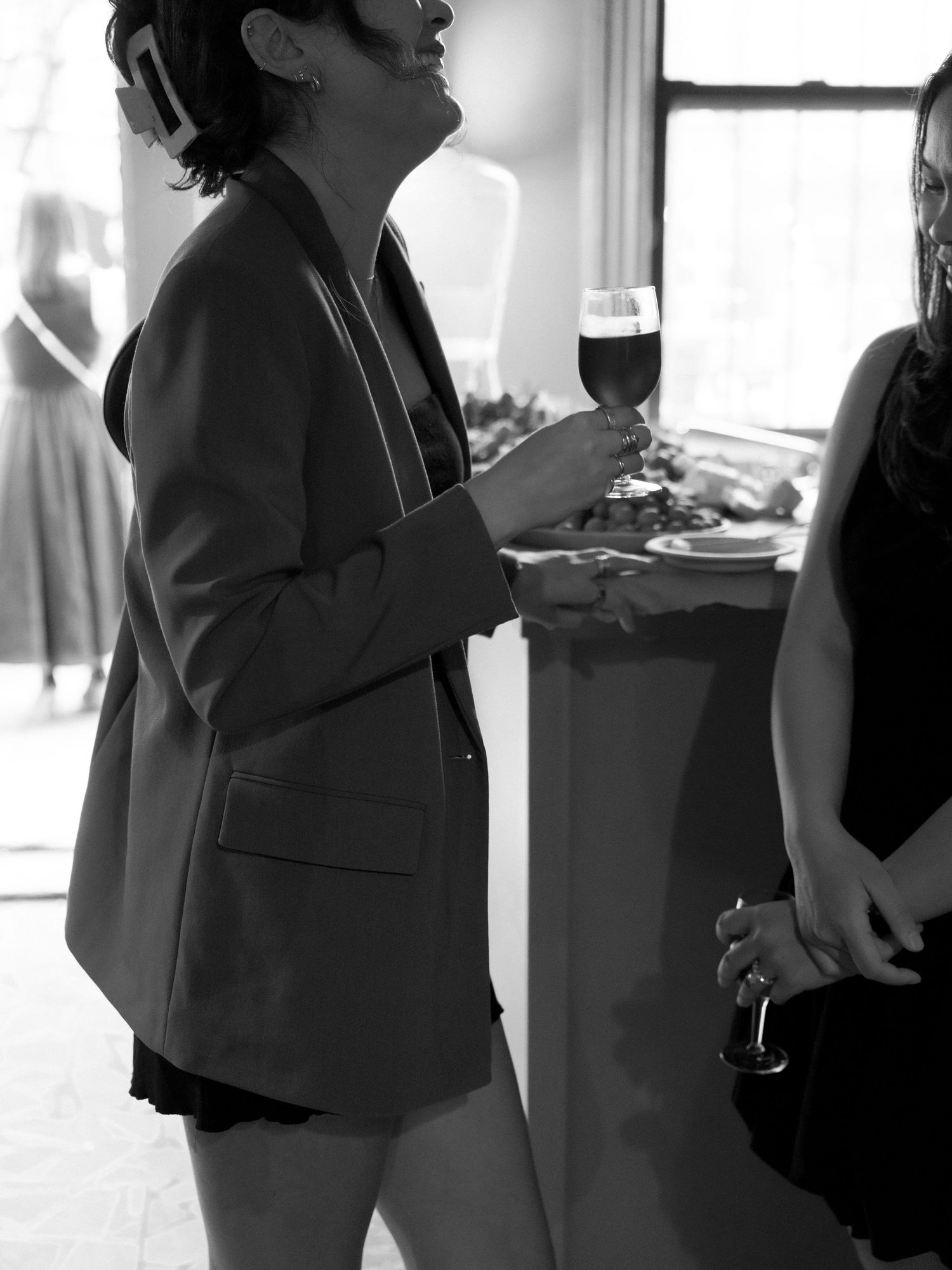 Indoor social gathering with people conversing in formal attire, shot in black and white.