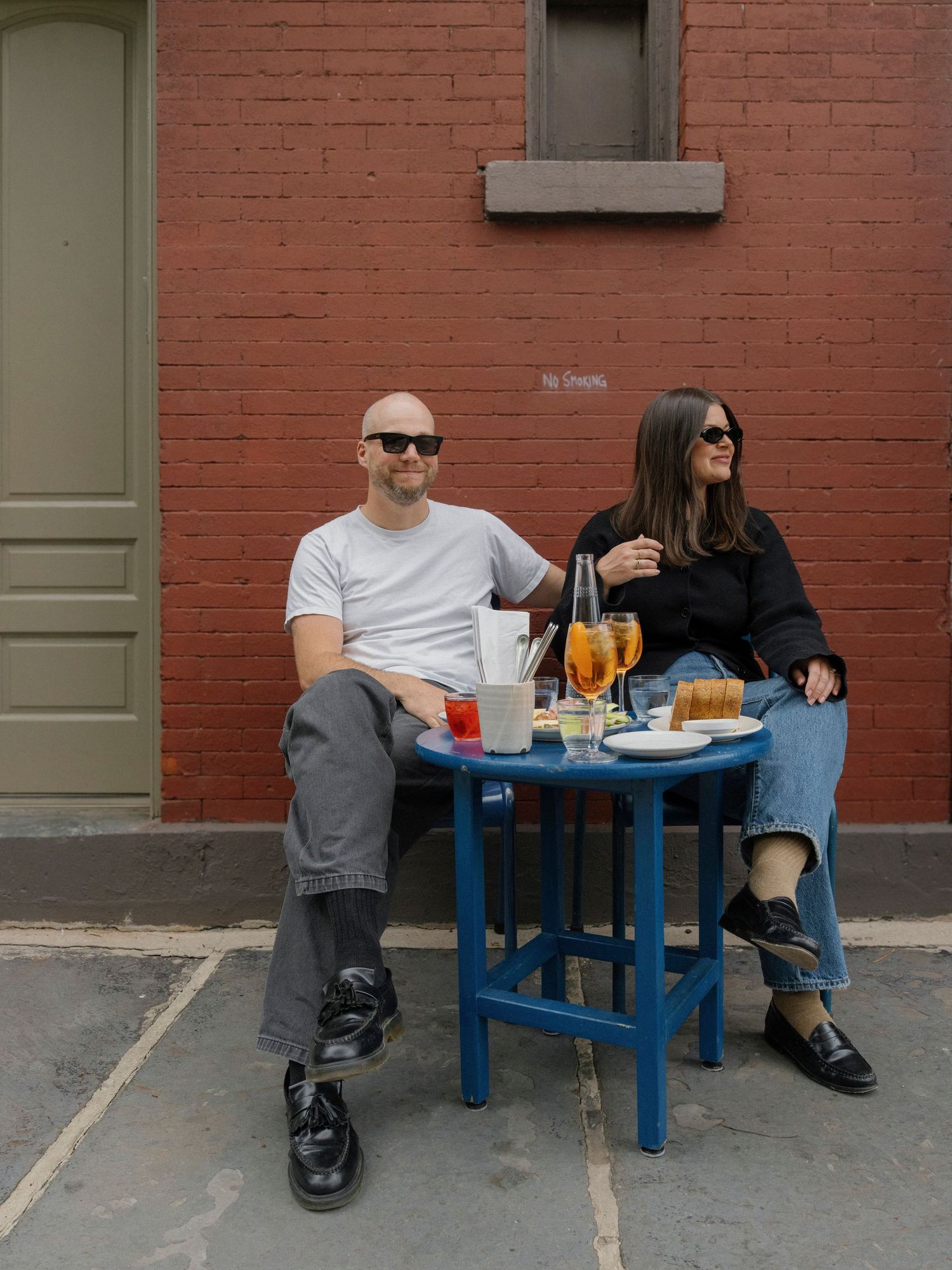Couple sitting at a blue outdoor table against a red brick wall.