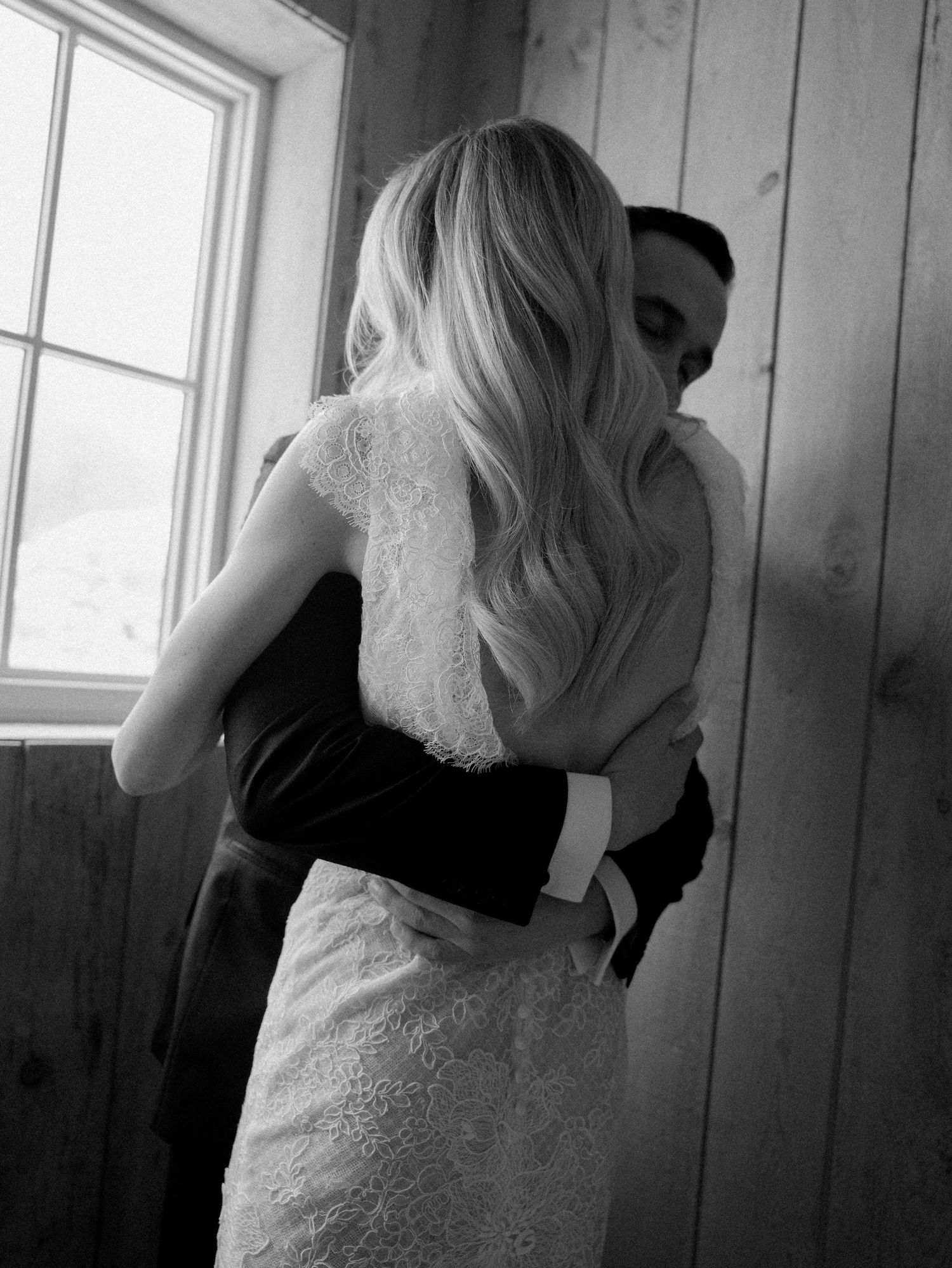 Close-up details of a white lace wedding dress against wooden paneled walls.