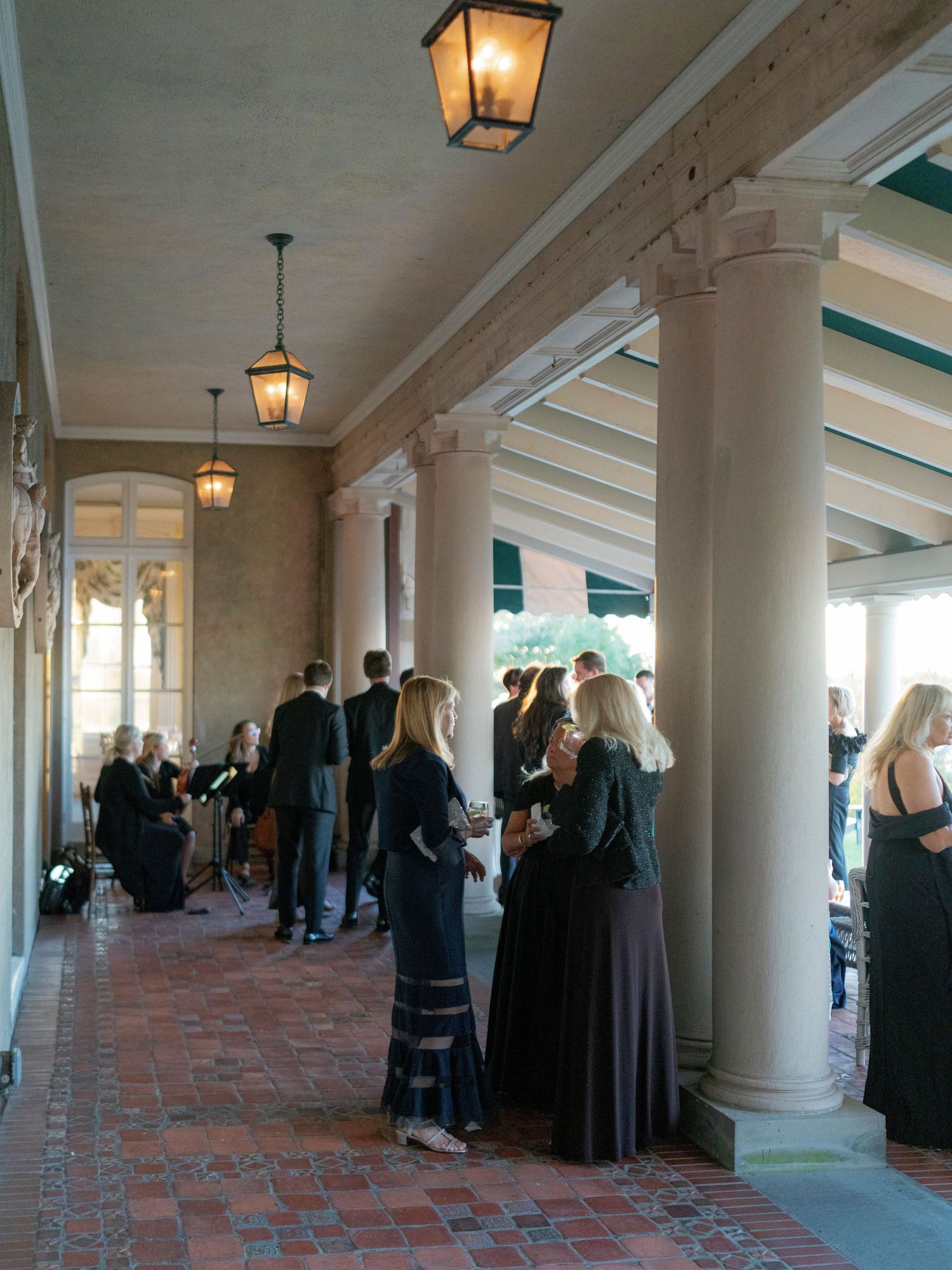 Wedding guests gather under lantern-lit columns during an evening reception.