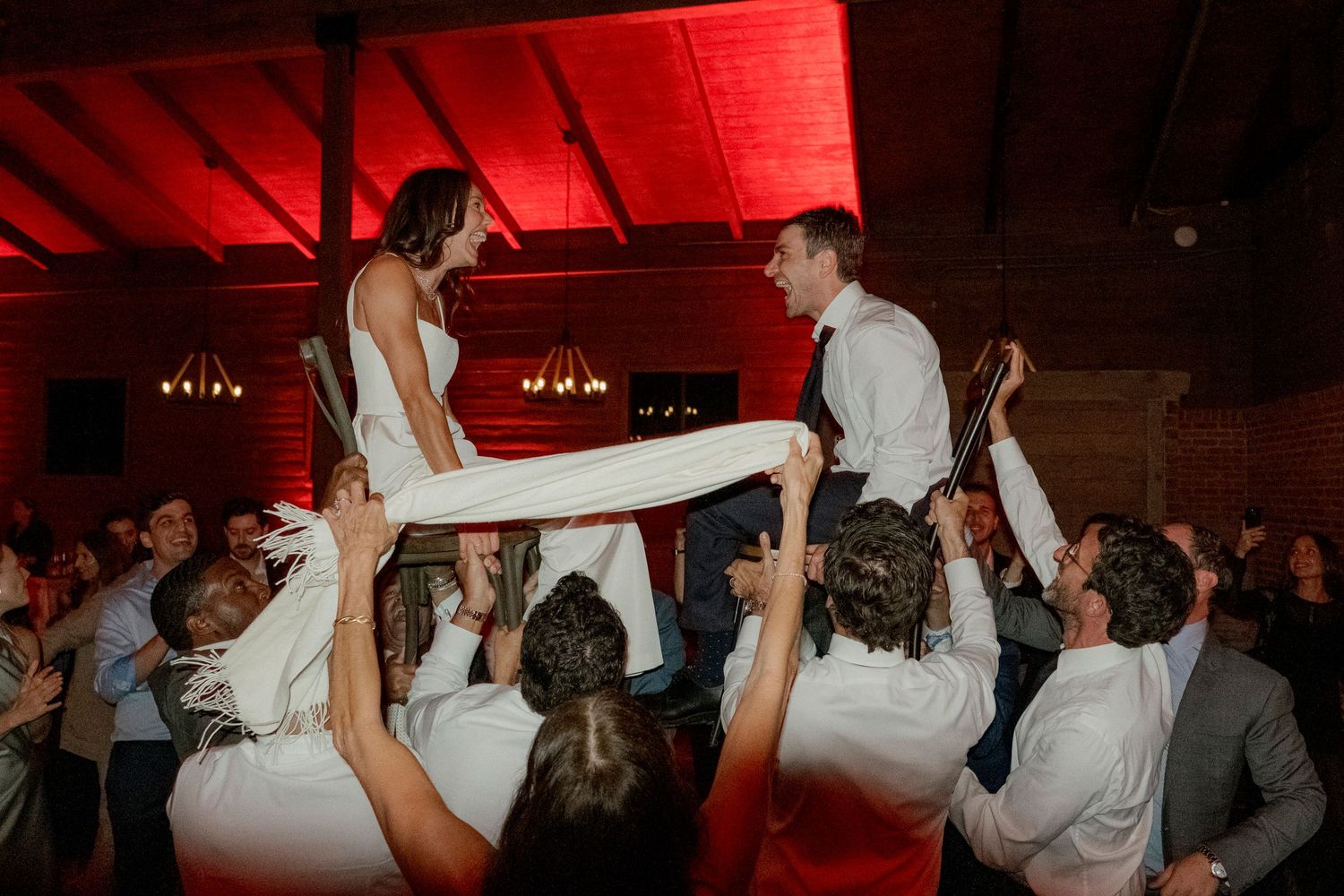 Wedding celebration on a dance floor with guests lifting and carrying others in celebration.