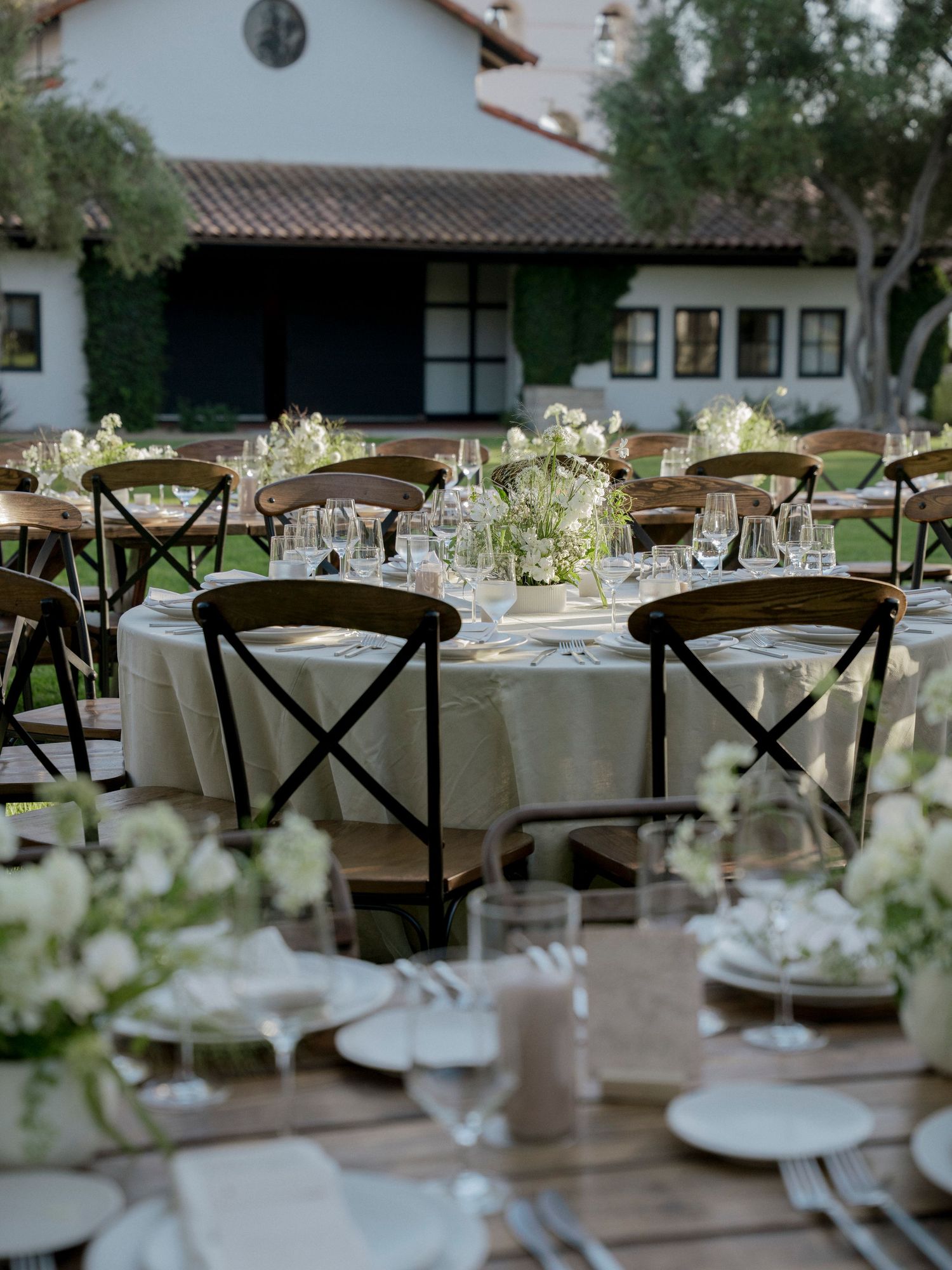 Elegant wedding reception tables set with cross-back chairs and white floral centerpieces.