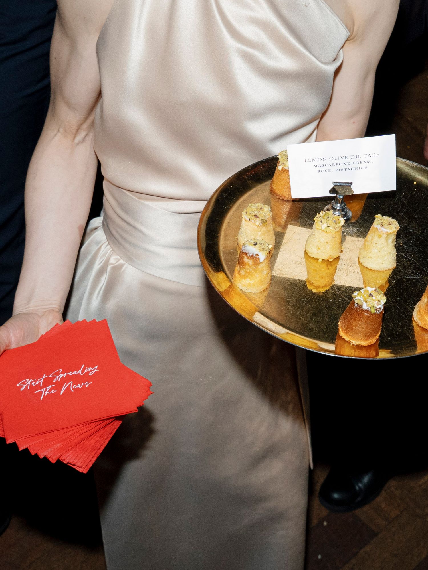 Server in white dress holding appetizers on a gold tray with red cocktail napkins.