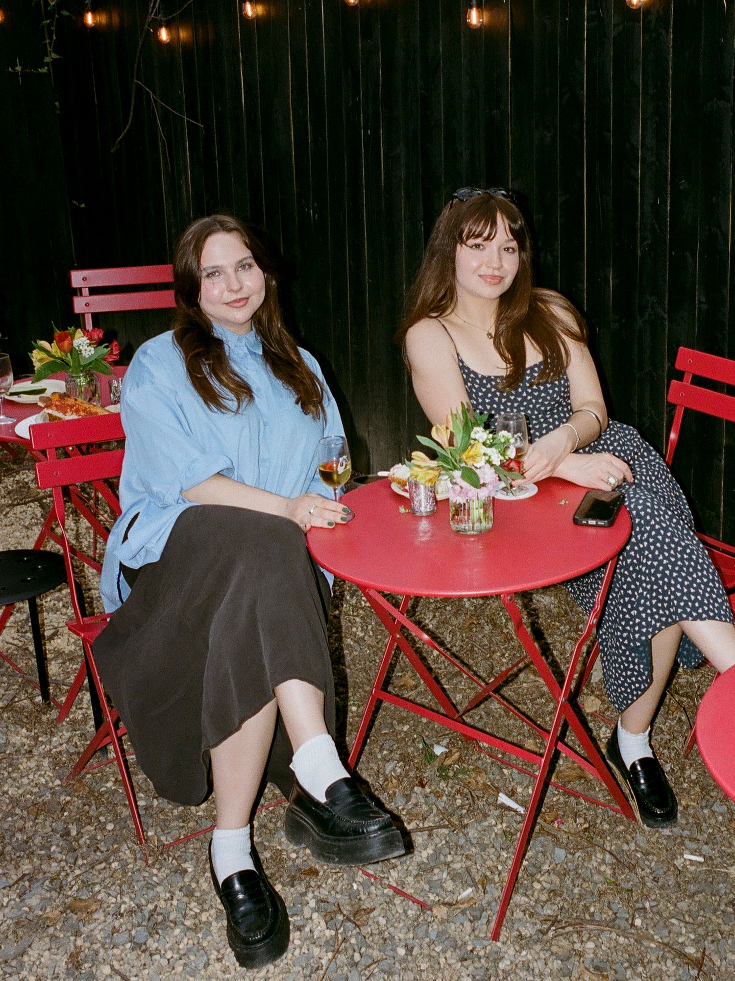 Friends relaxing at outdoor tables with drinks and floral centerpieces.