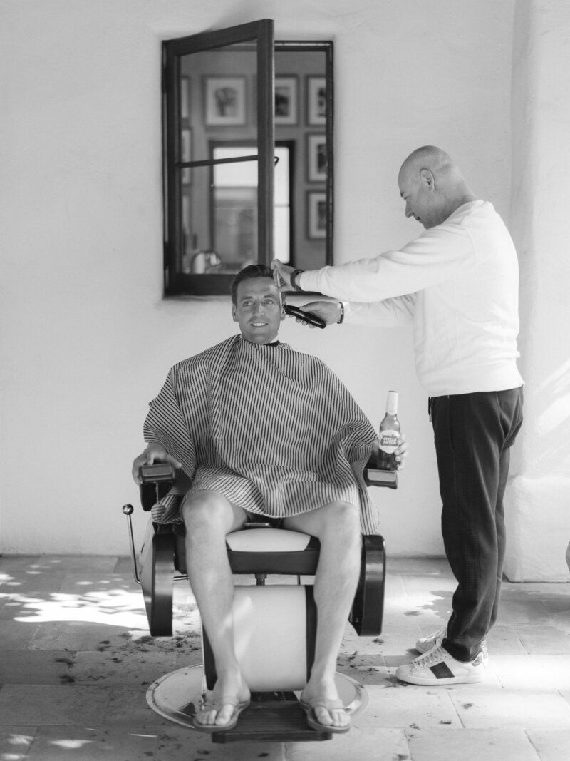 A barbershop scene in black and white showing a haircut in progress.