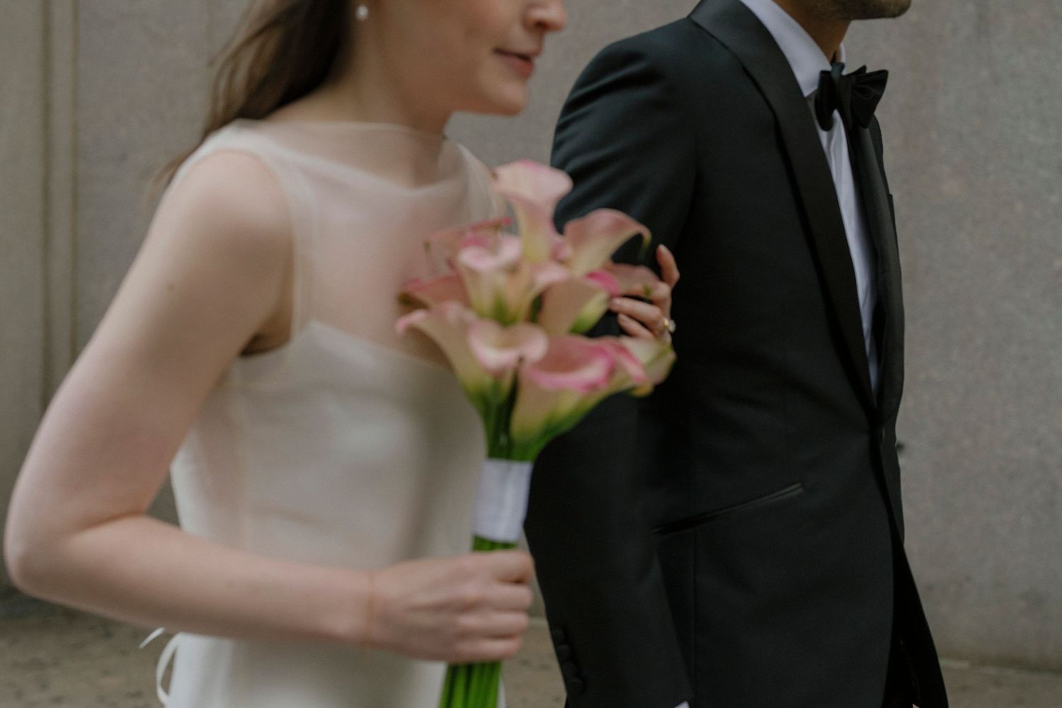 A romantic wedding couple shares an intimate moment while posing for photos against a stone wall backdrop.
