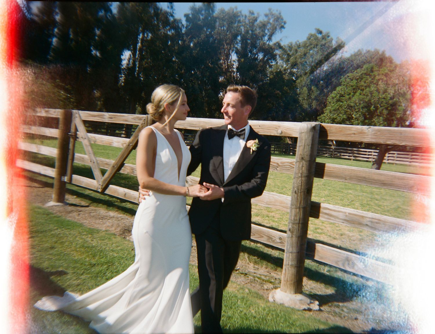 Wedding couple posing together on a sunny day near a wooden fence.