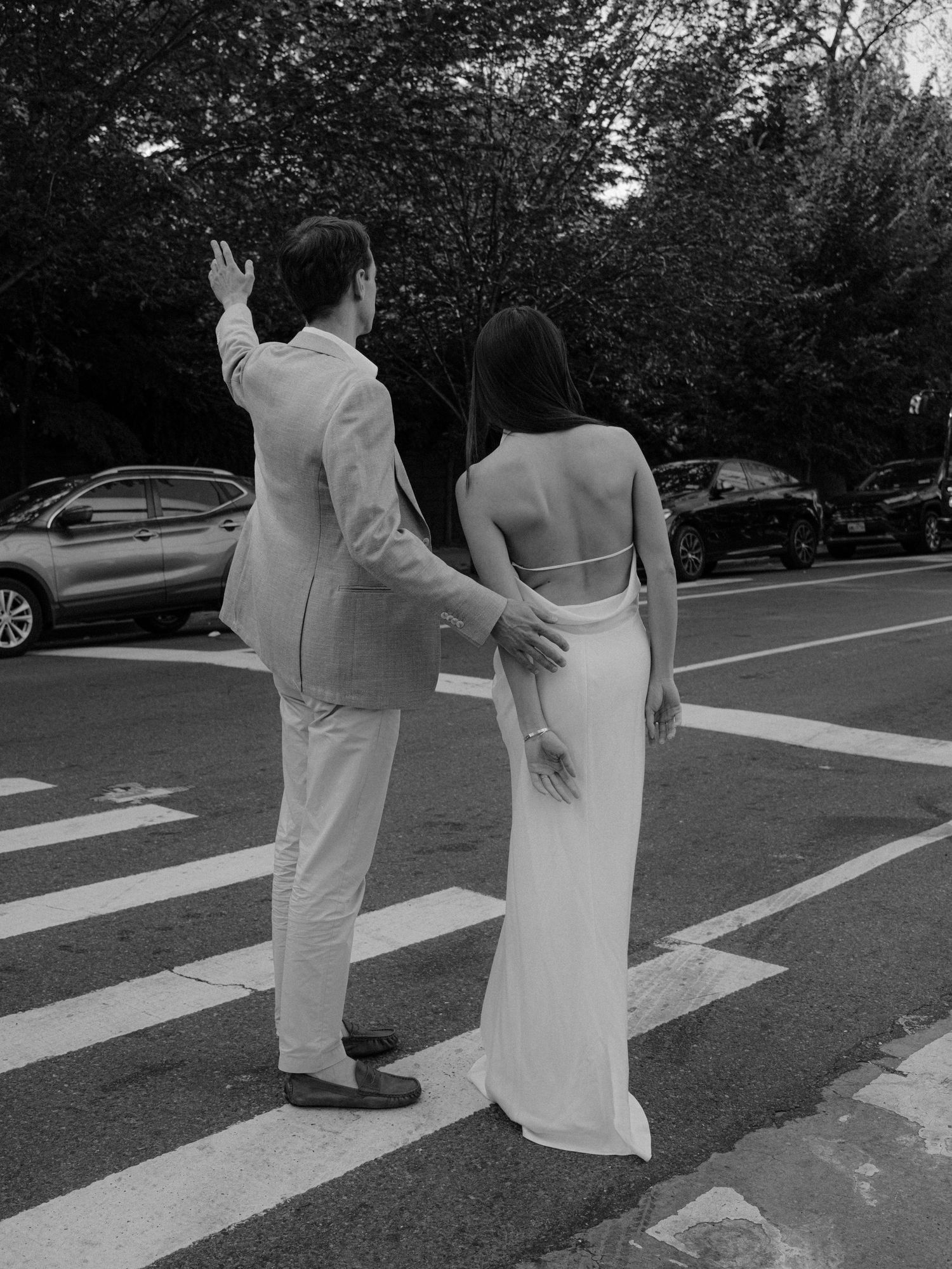 Black and white photo of a couple walking across a crosswalk in formal attire.