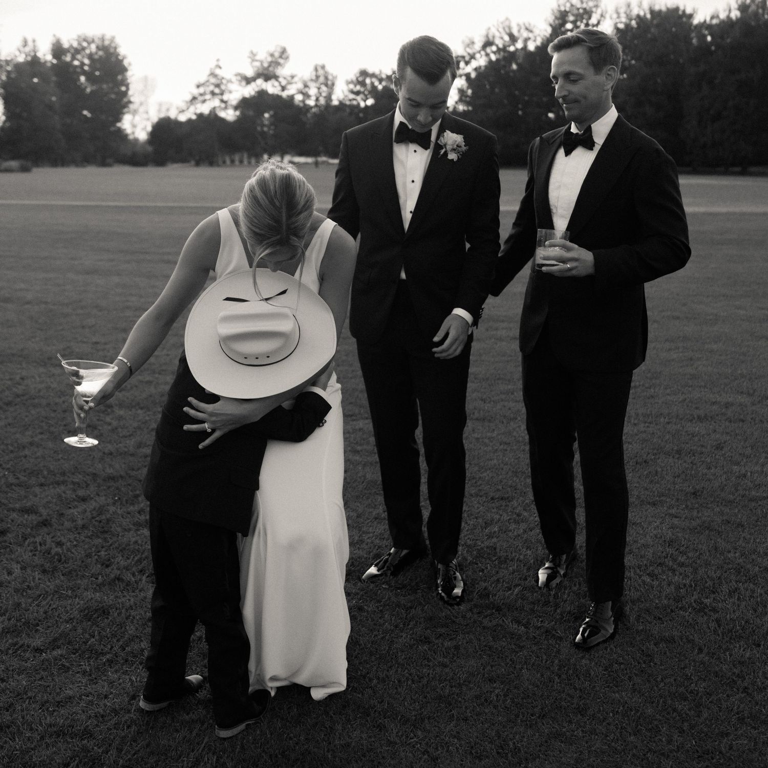 Wedding party in formal attire walking across an outdoor field at dusk.