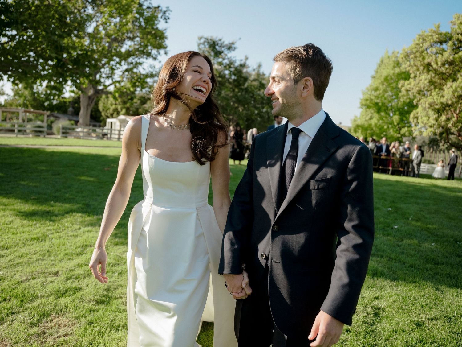 Happy couple sharing a candid laughing moment on their wedding day in a sunny garden.