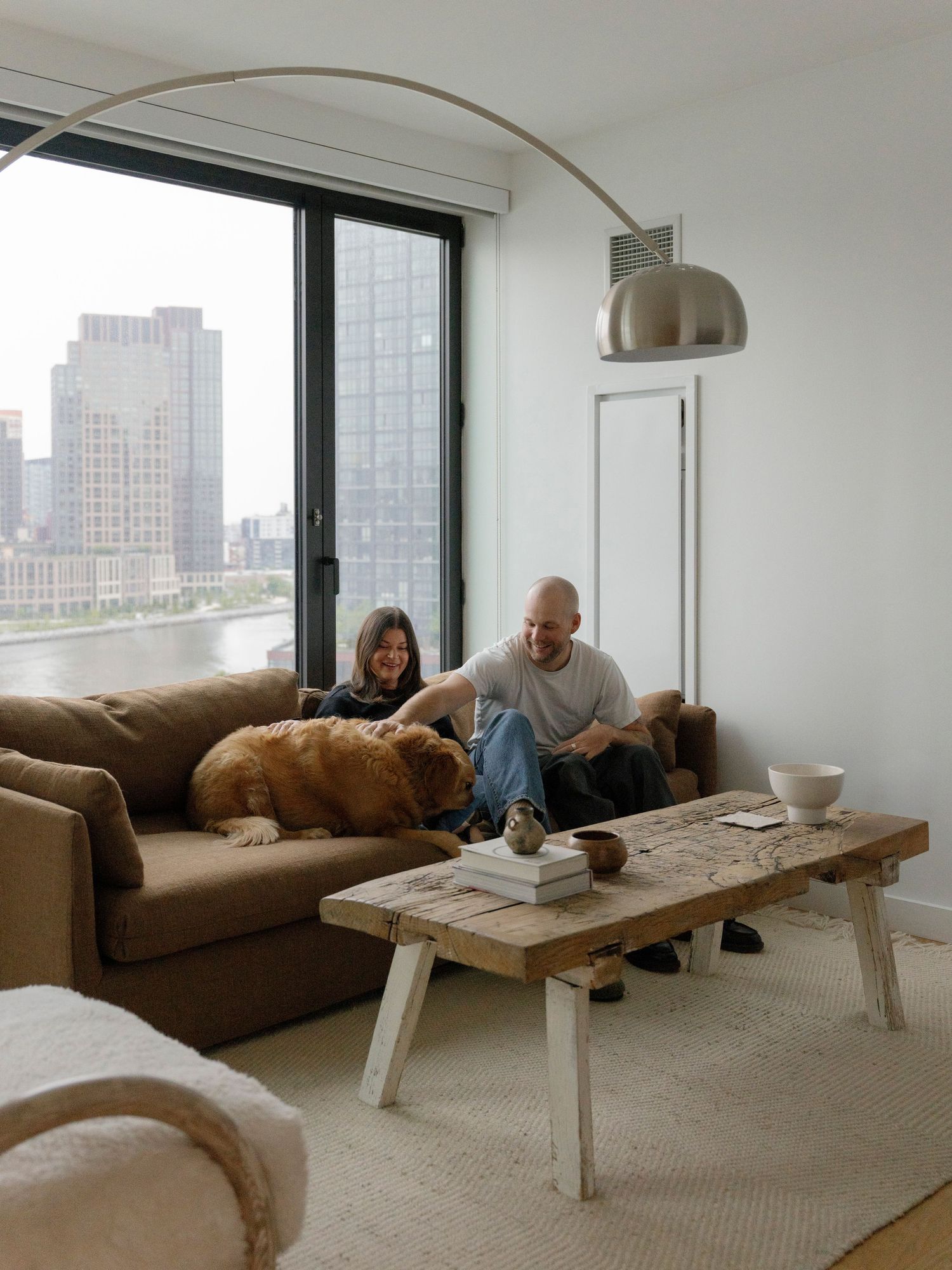 Modern apartment living room with city views and people relaxing on brown couch.
