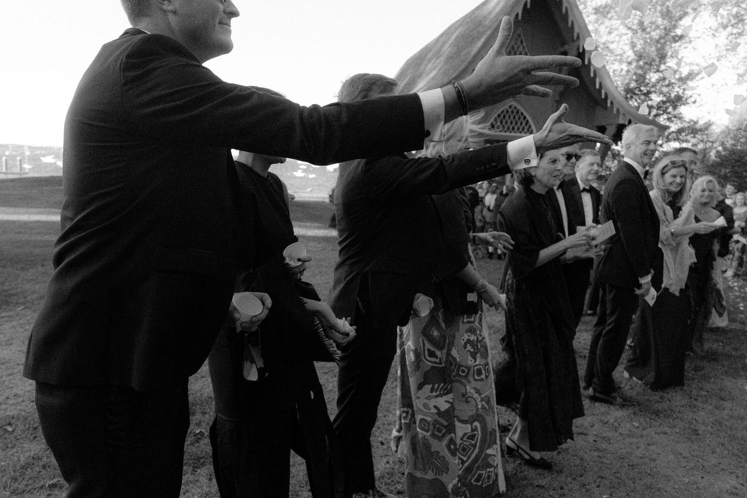 Wedding guests toss flower petals at the newlyweds during an outdoor celebration.