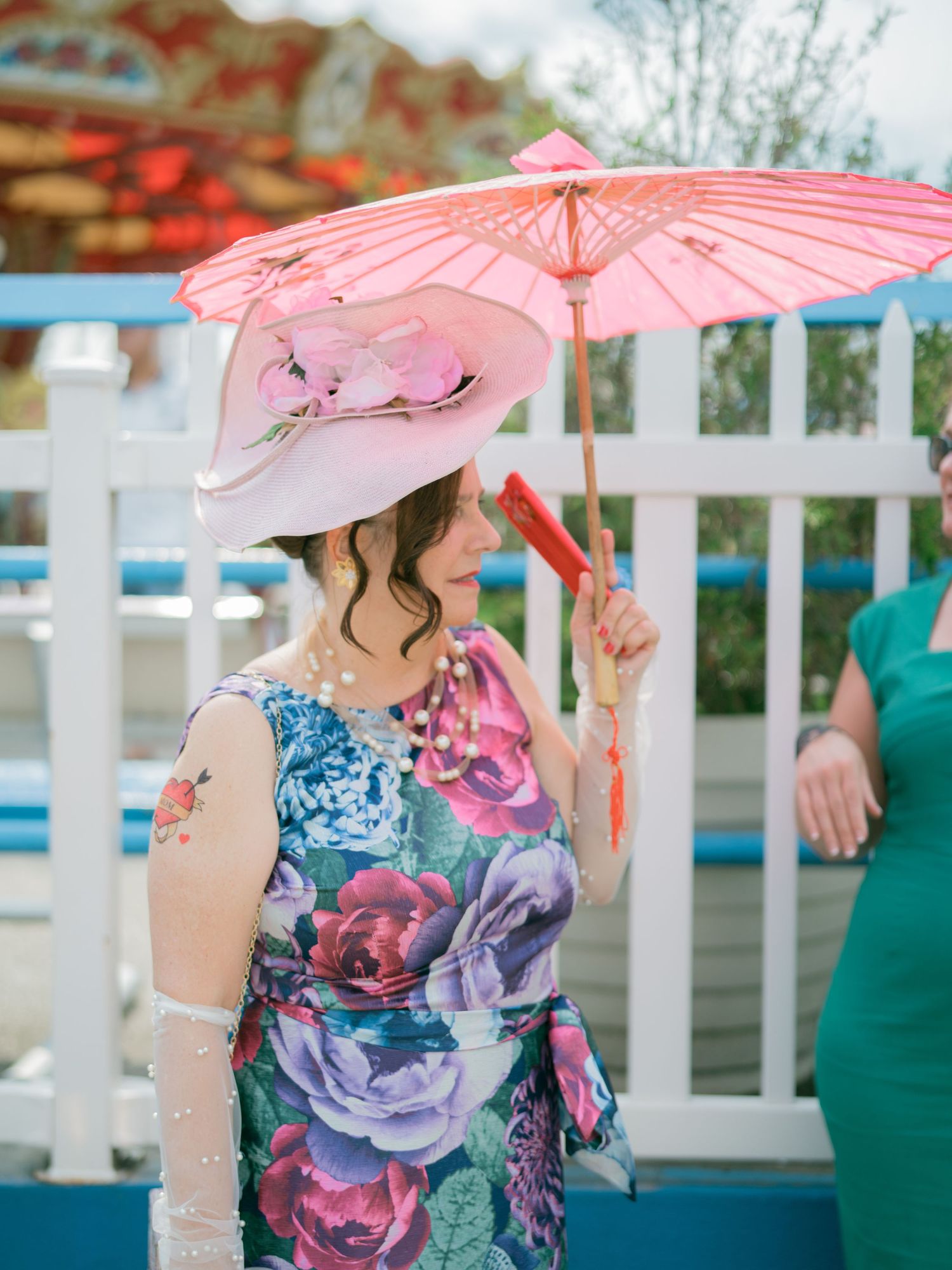 Pink parasol and floral dress details against white picket fence backdrop.