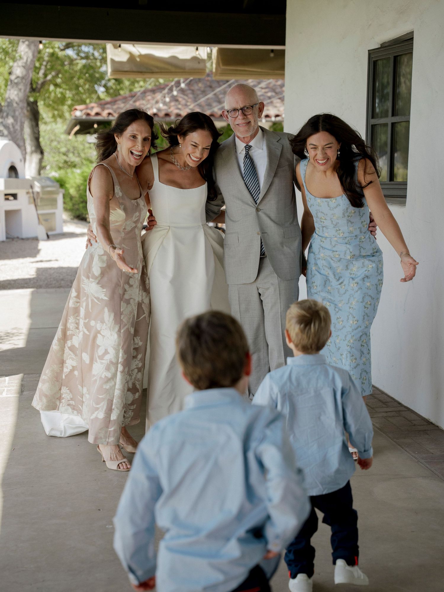 Joyful wedding party walking together on a covered porch with two children in foreground.