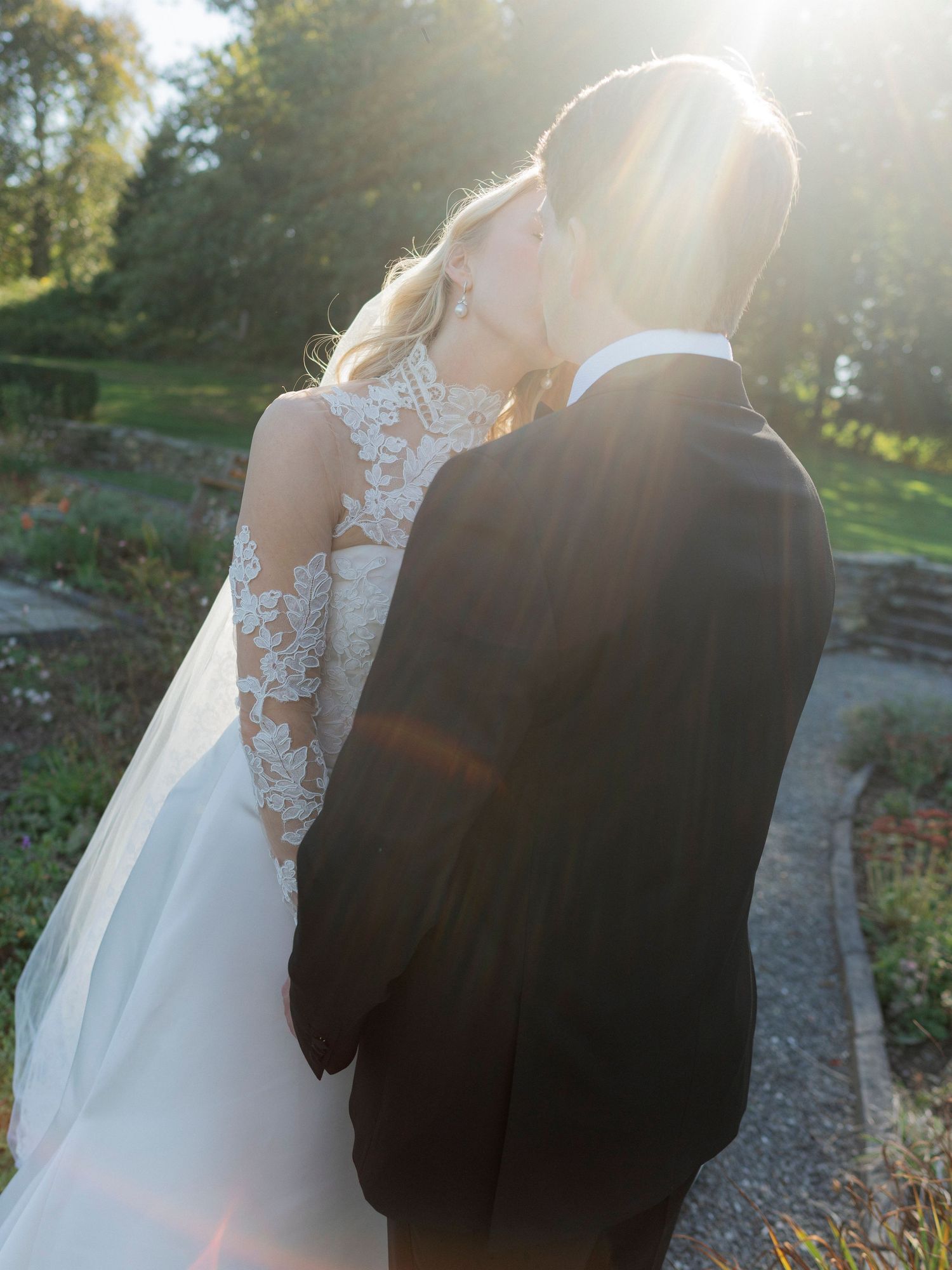 Romantic sunset wedding photo with sunflare highlighting the couple's silhouette outdoors.