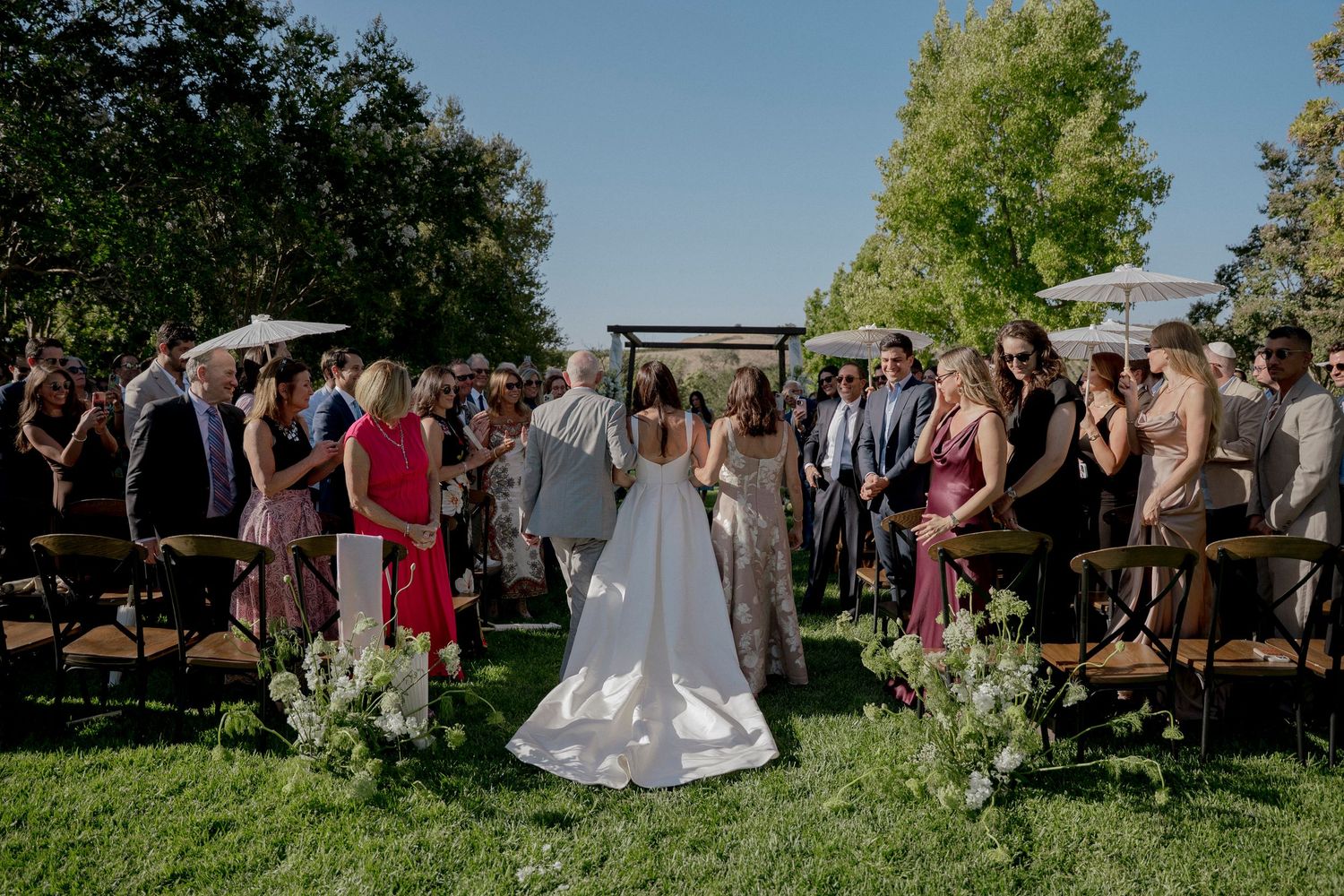 An outdoor wedding ceremony setup with guests seated on wooden benches surrounded by greenery.