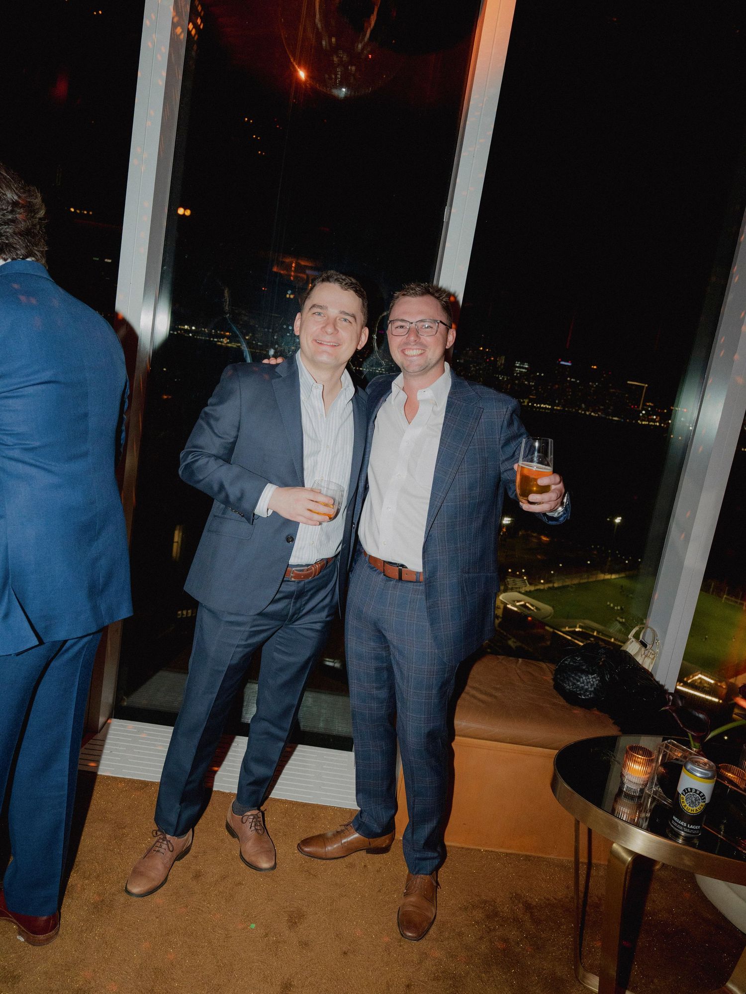 Evening celebration with guests enjoying drinks by large windows overlooking city lights.