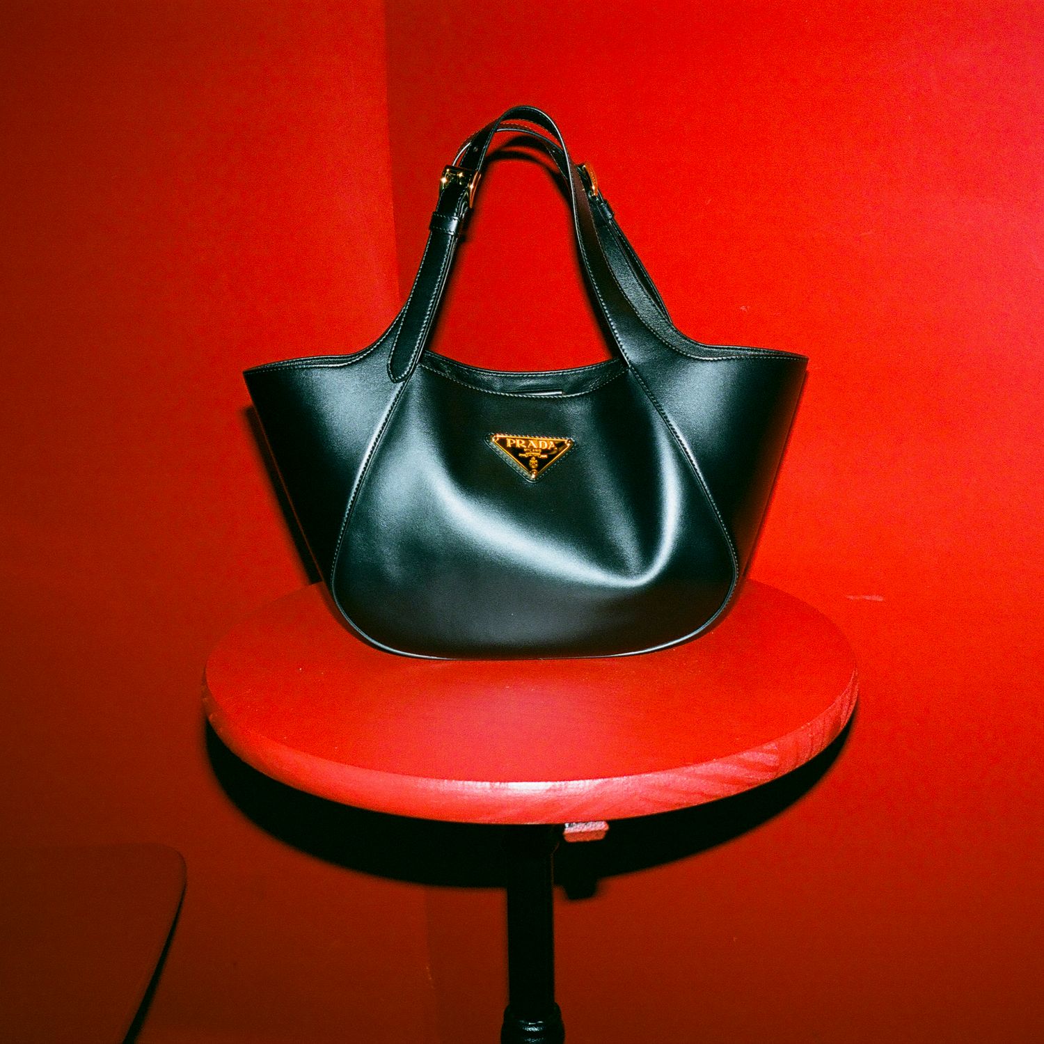 Black leather handbag displayed on red background in multiple angles.