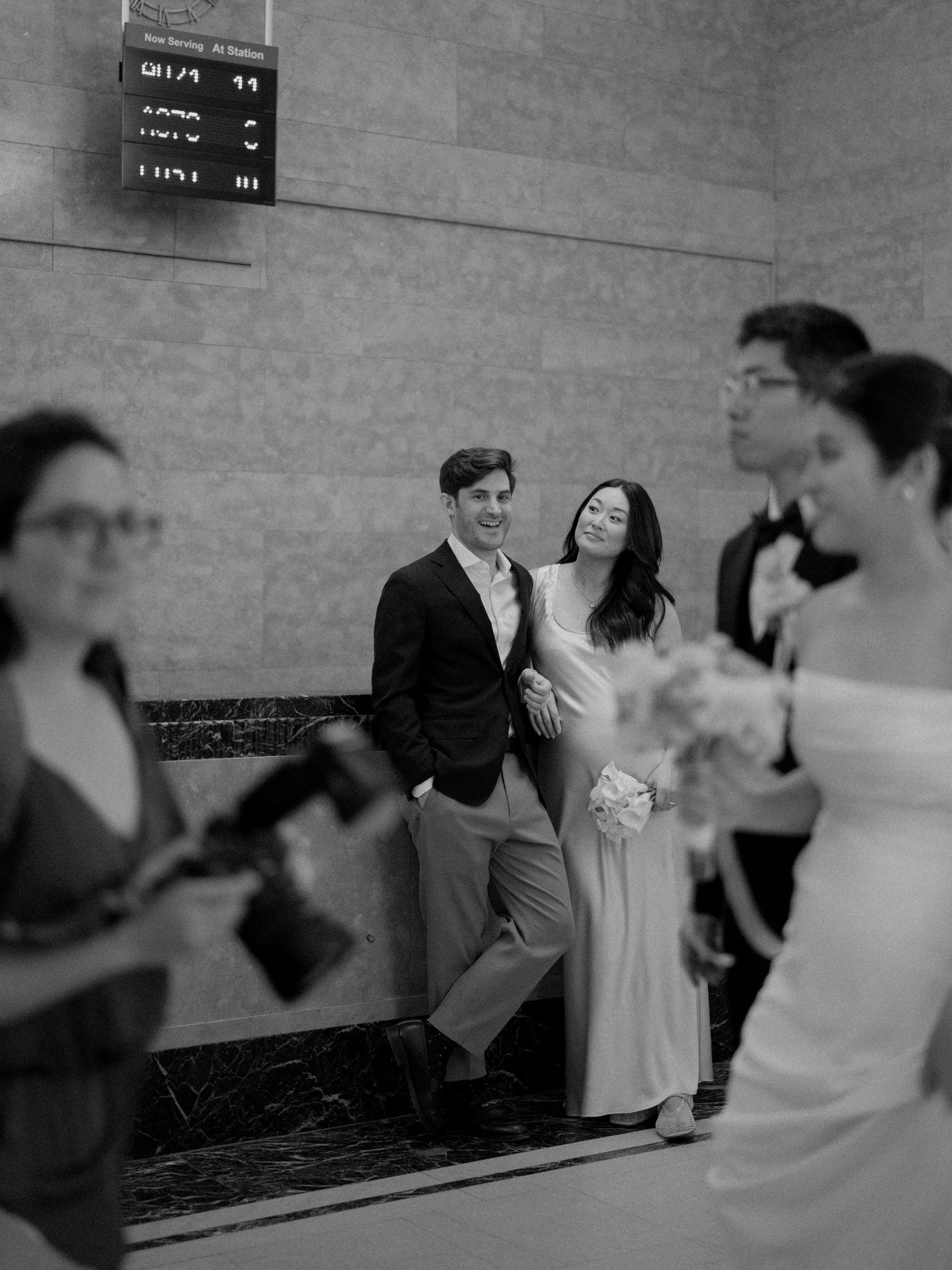 A candid black and white moment captured in a marble-walled venue with others nearby.