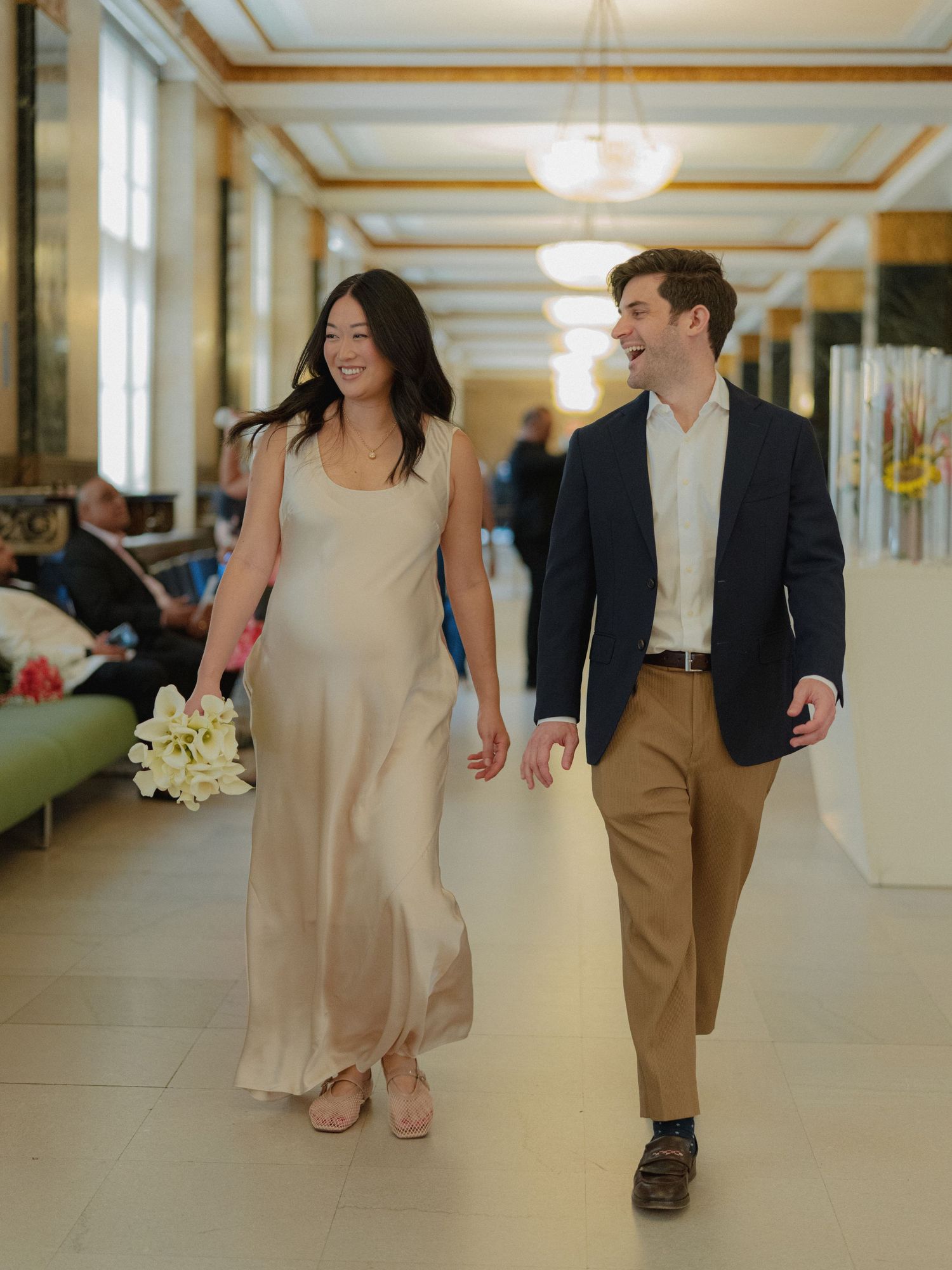 Couple walking through a bright hallway with cream colored walls and ornate molding.