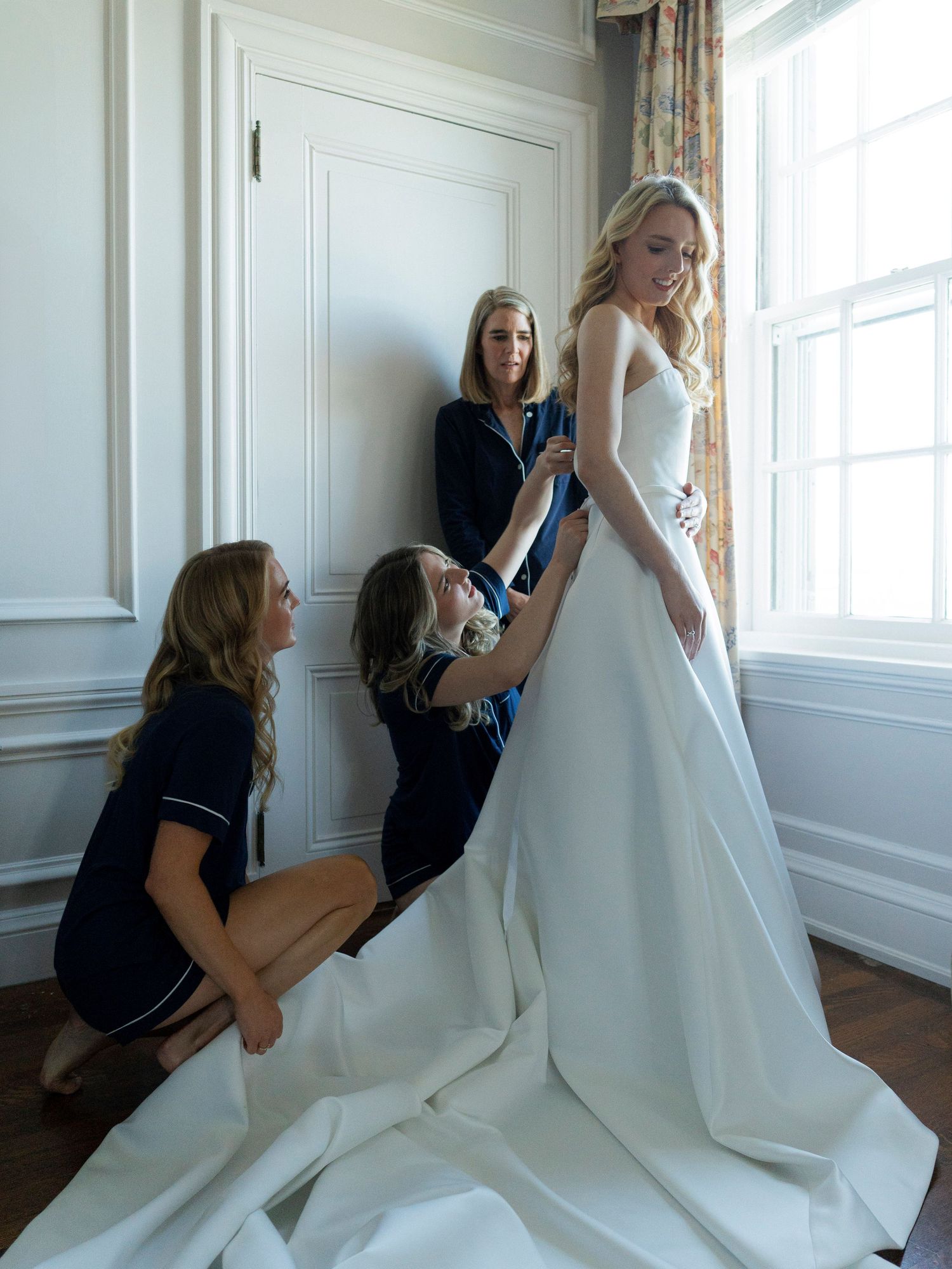 Wedding dress being adjusted and fitted by assistants in bright room.