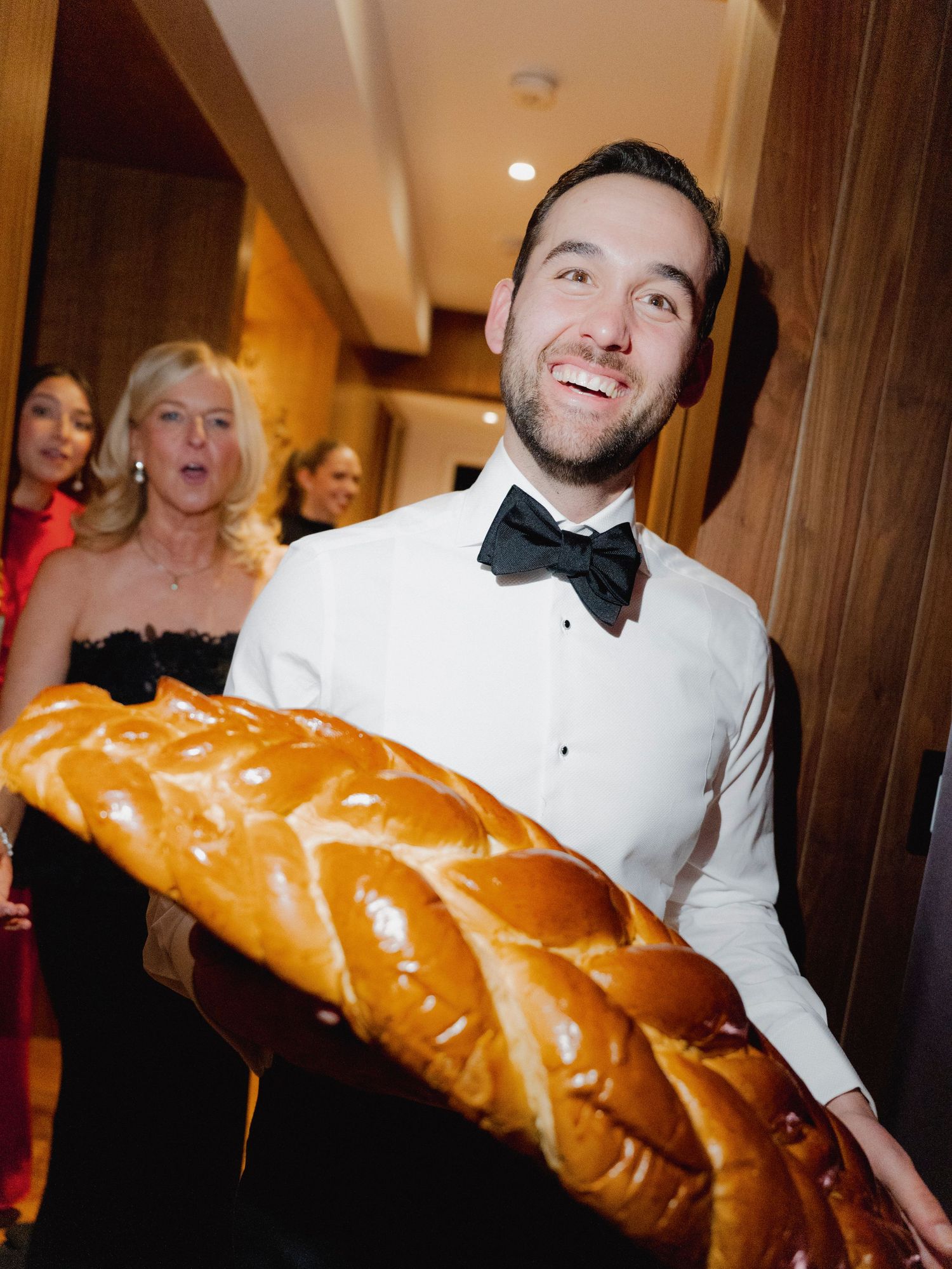 Wedding party members playfully posing with a giant ceremonial challah bread at a reception.
