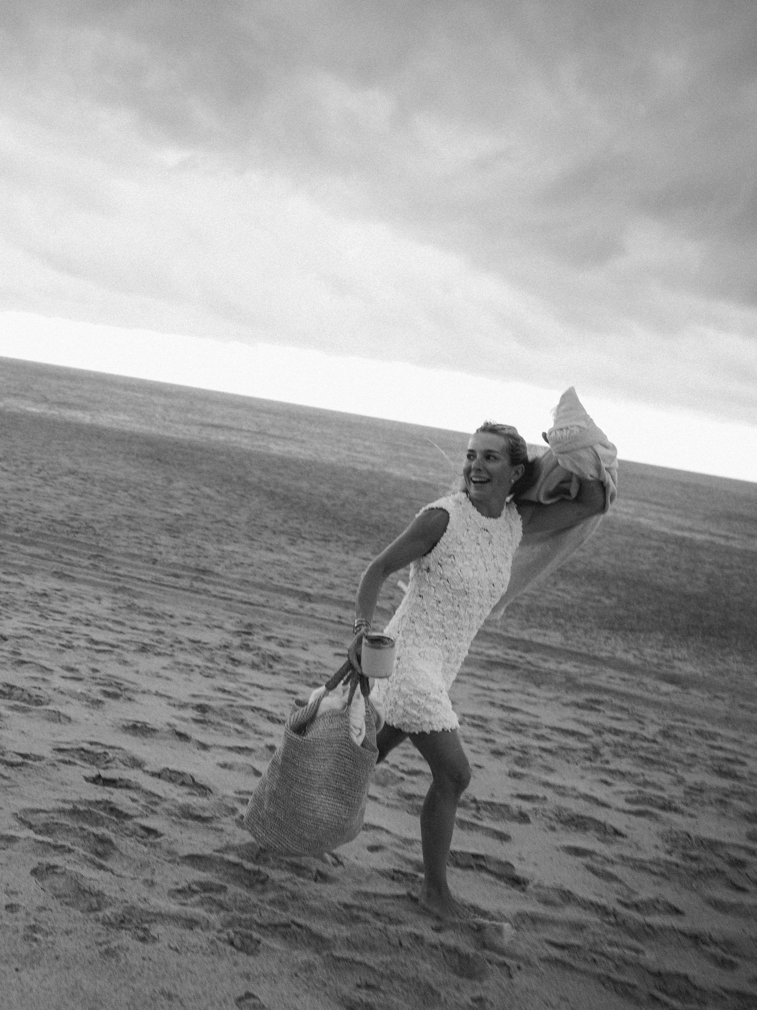 Black and white photo sequence of a person jumping and twirling on a beach with dramatic cloudy skies.