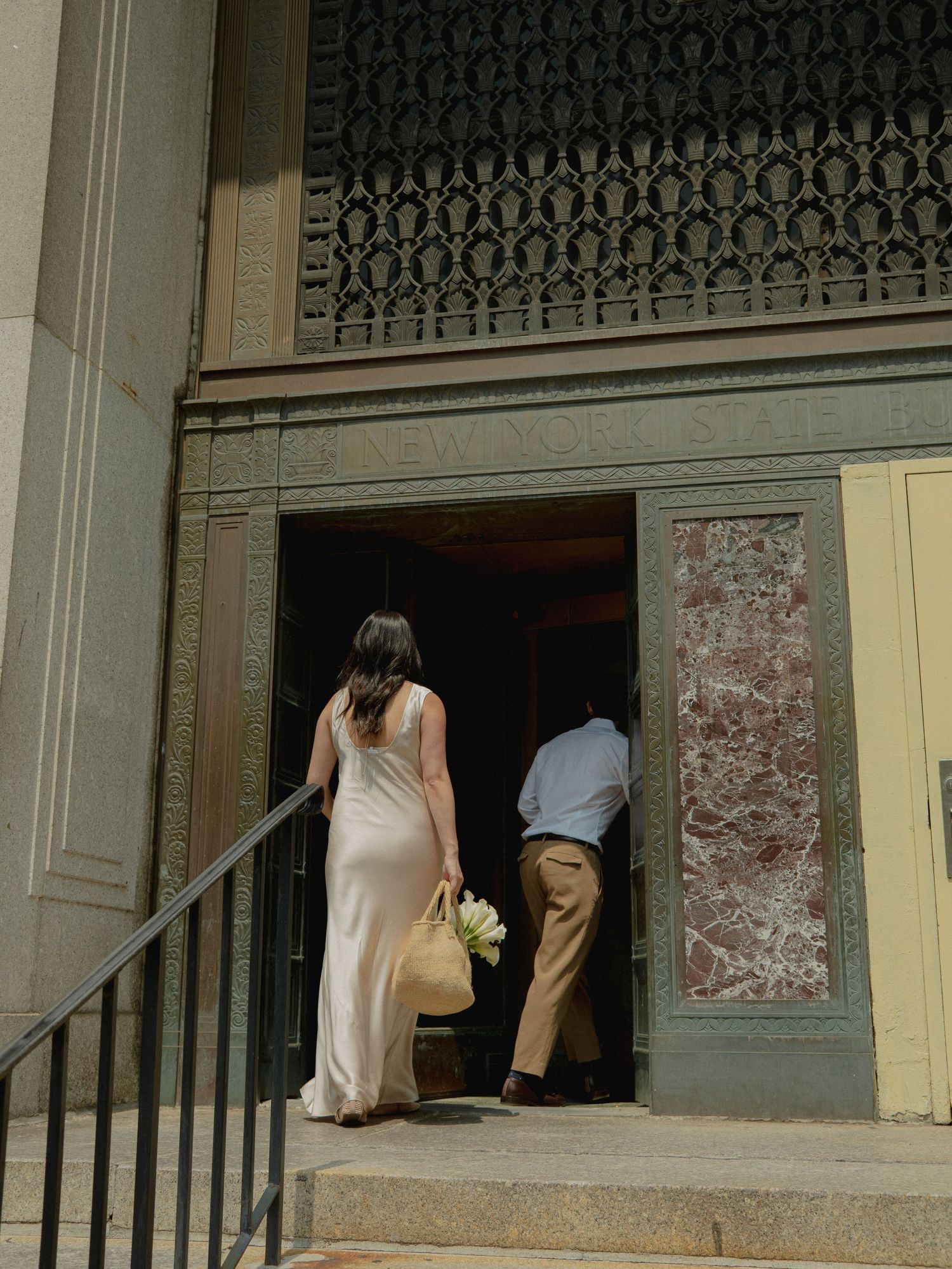 A couple enters a historic building through ornate doors with decorative ironwork above.