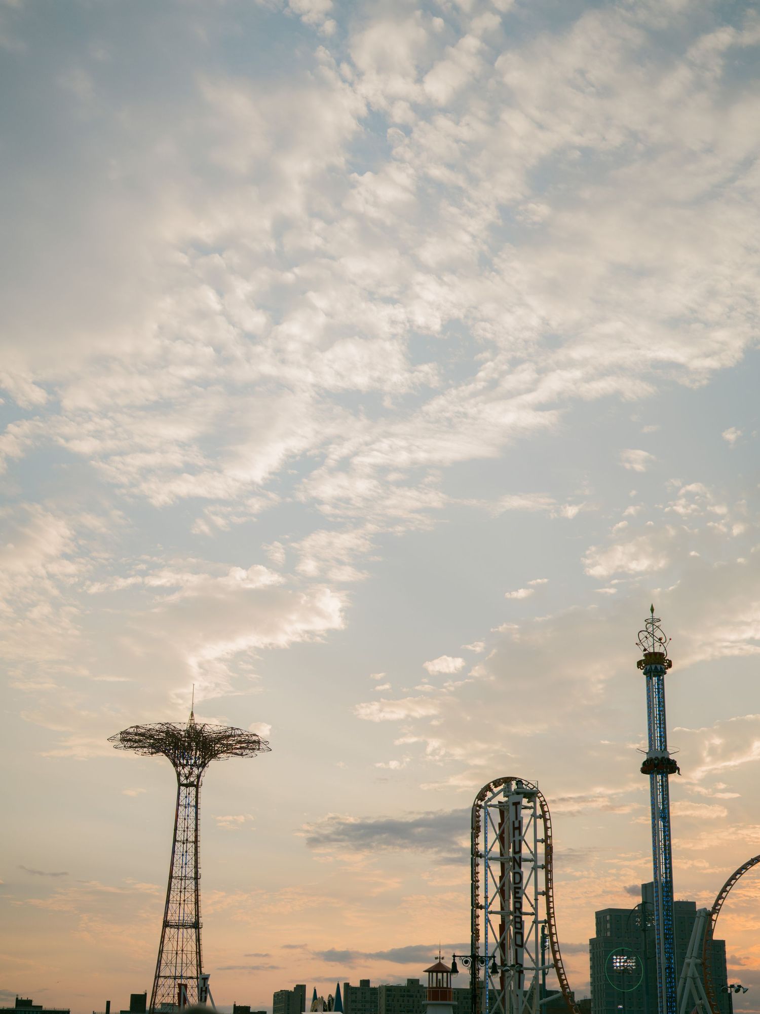 Silhouette of amusement park rides and attractions against a cloudy sunset sky.