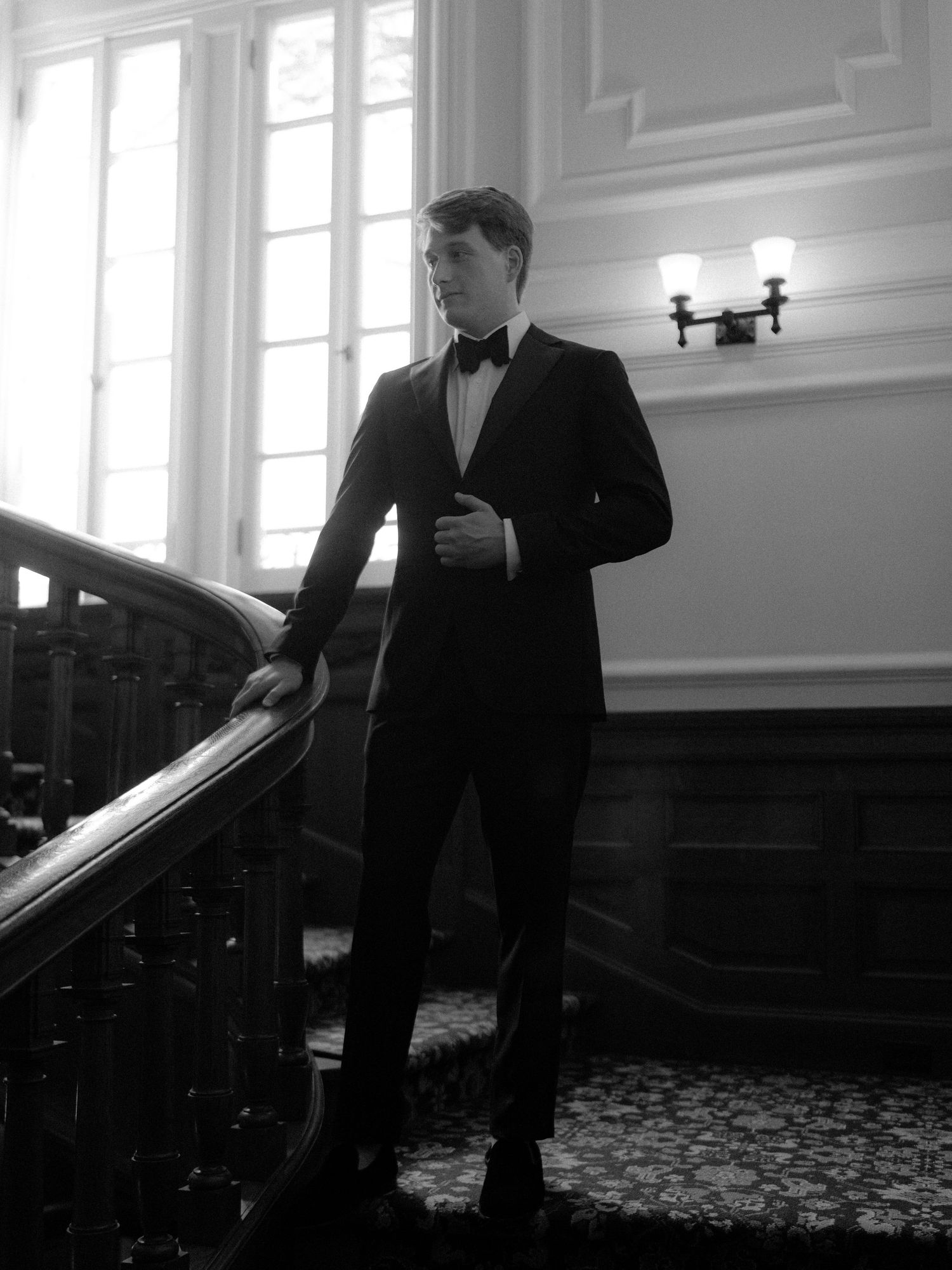 Artistic black and white series showing a person in formal attire walking through an elegant room with patterned carpet.