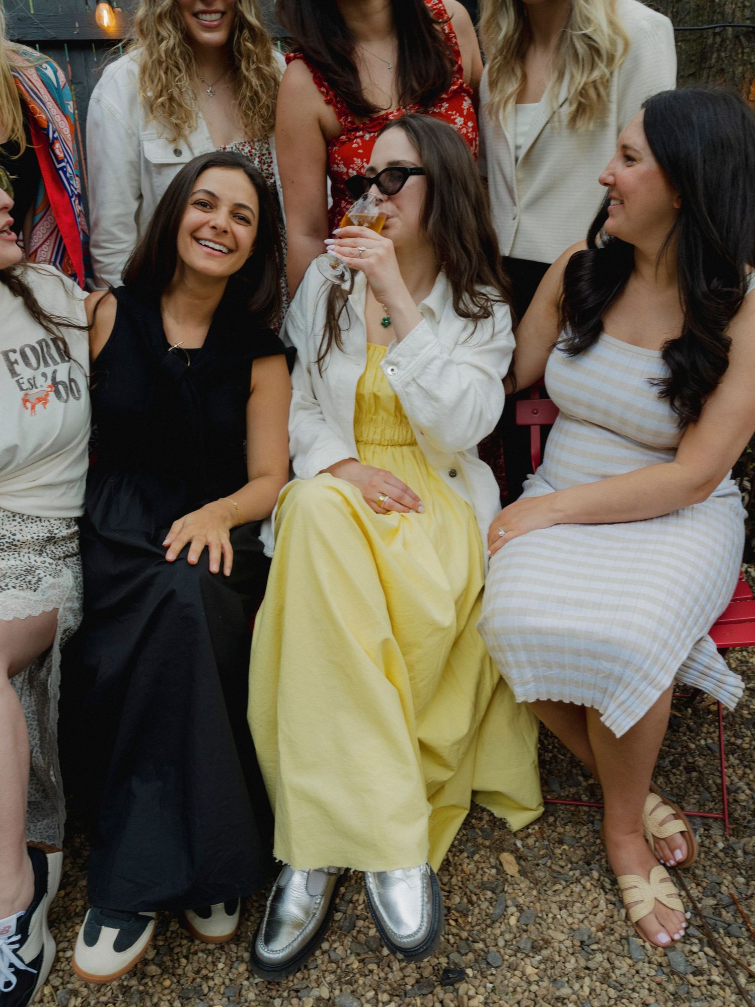 Group of friends sitting together outdoors wearing casual summer outfits.