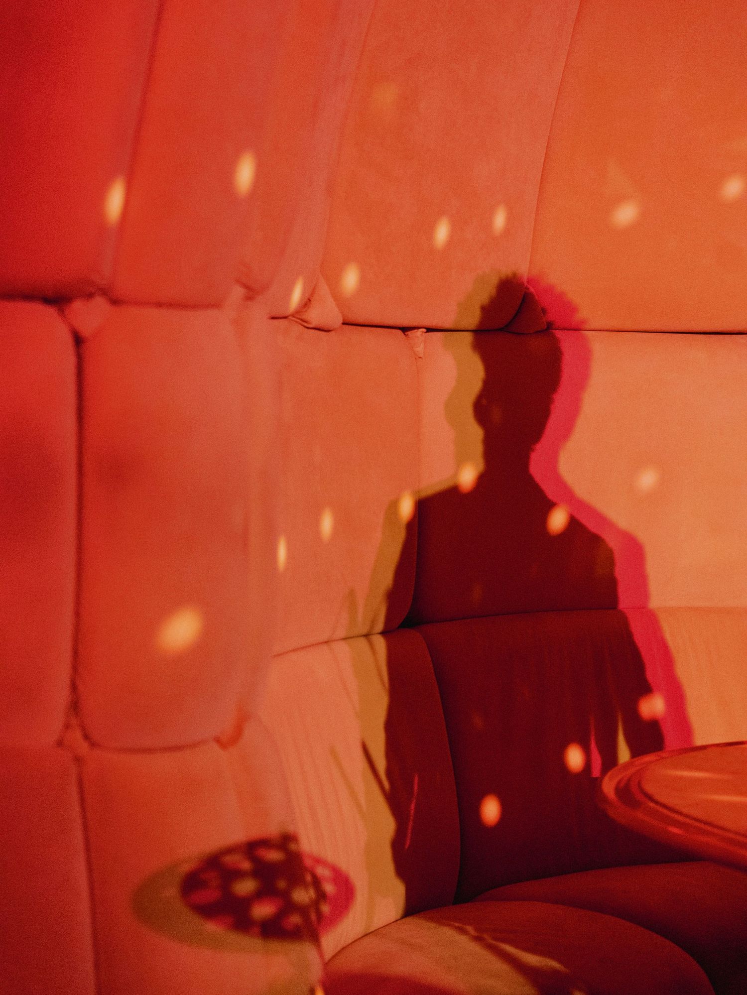 A silhouette against red-lit padded walls with disco light reflections.