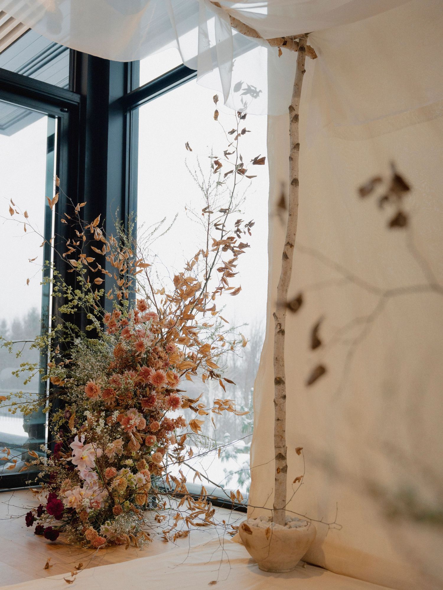 Autumn floral arrangement with birch branches by a window.