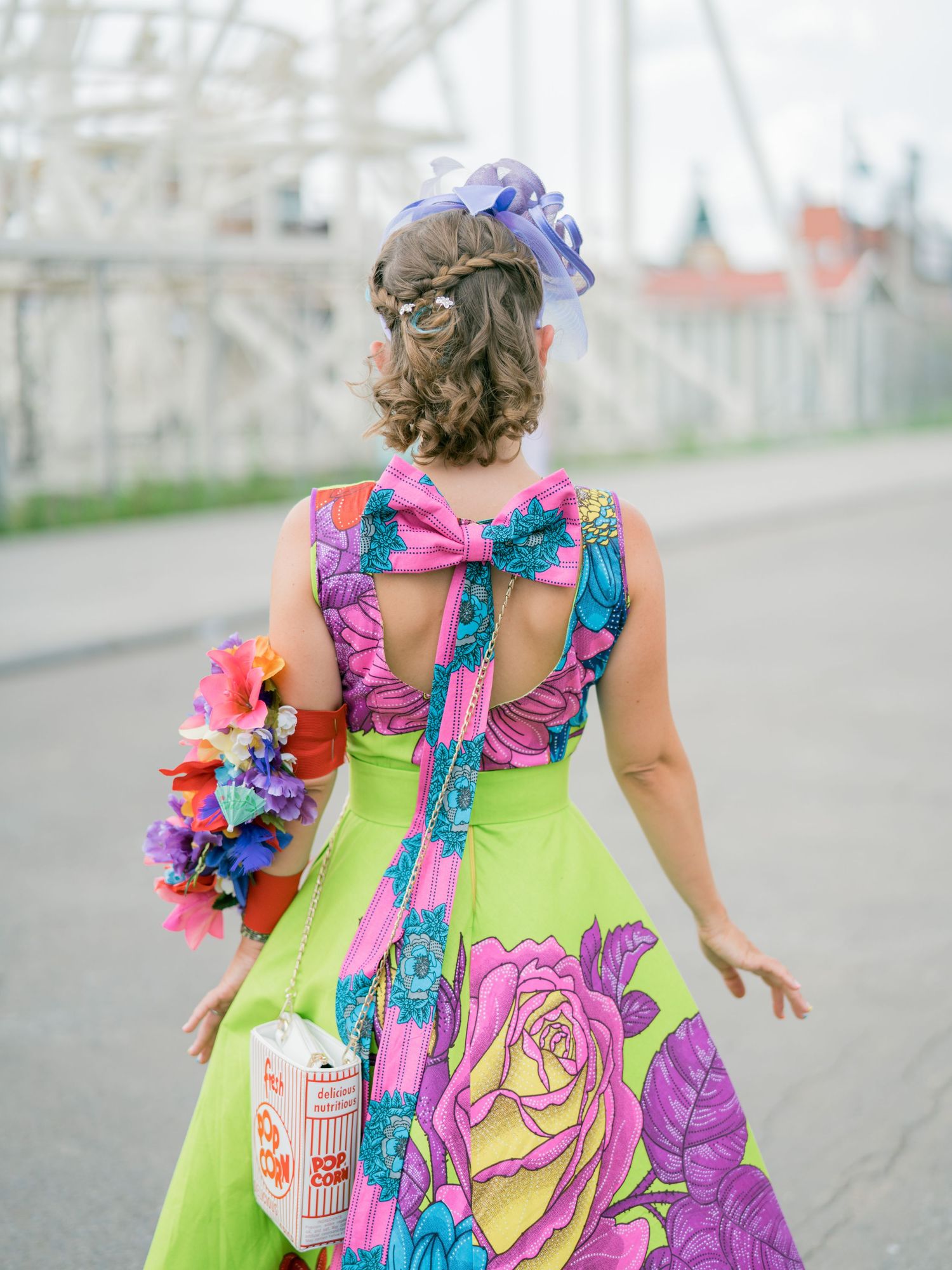A vibrant neon green dress with colorful floral accents and ruffles shown from behind on a boardwalk.