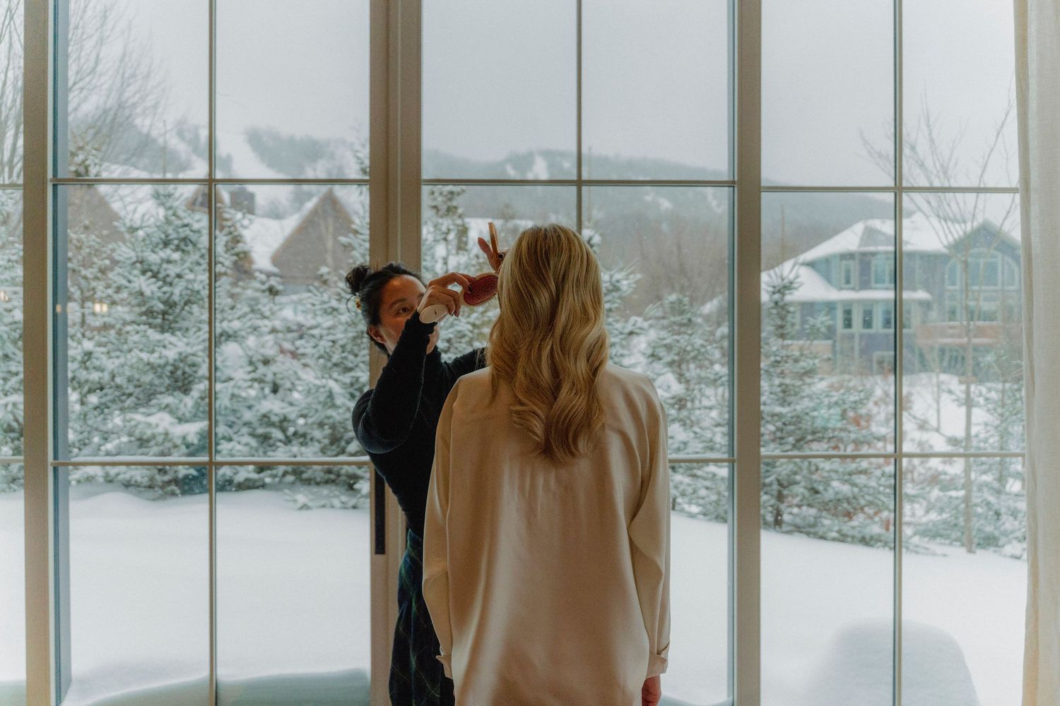 Snow-covered winter scene viewed through large windows of a modern building.