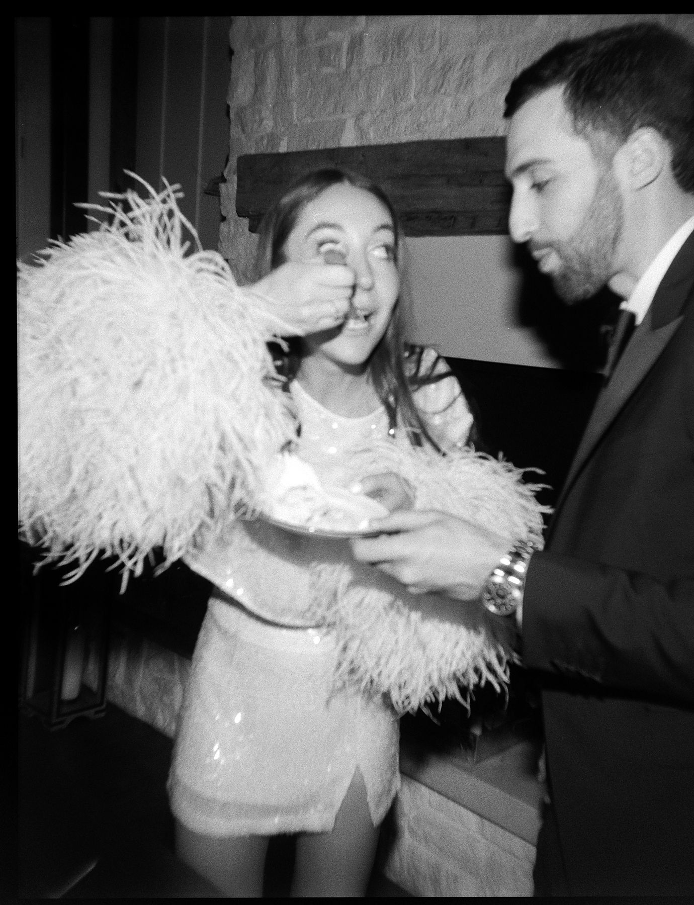 Party scene with people dancing and wearing feathered costumes in black and white.