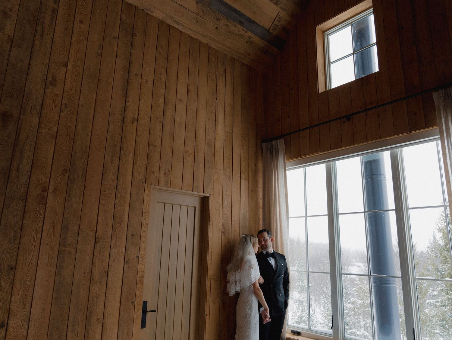 Interior of a rustic wooden cabin with large windows and natural light streaming in.