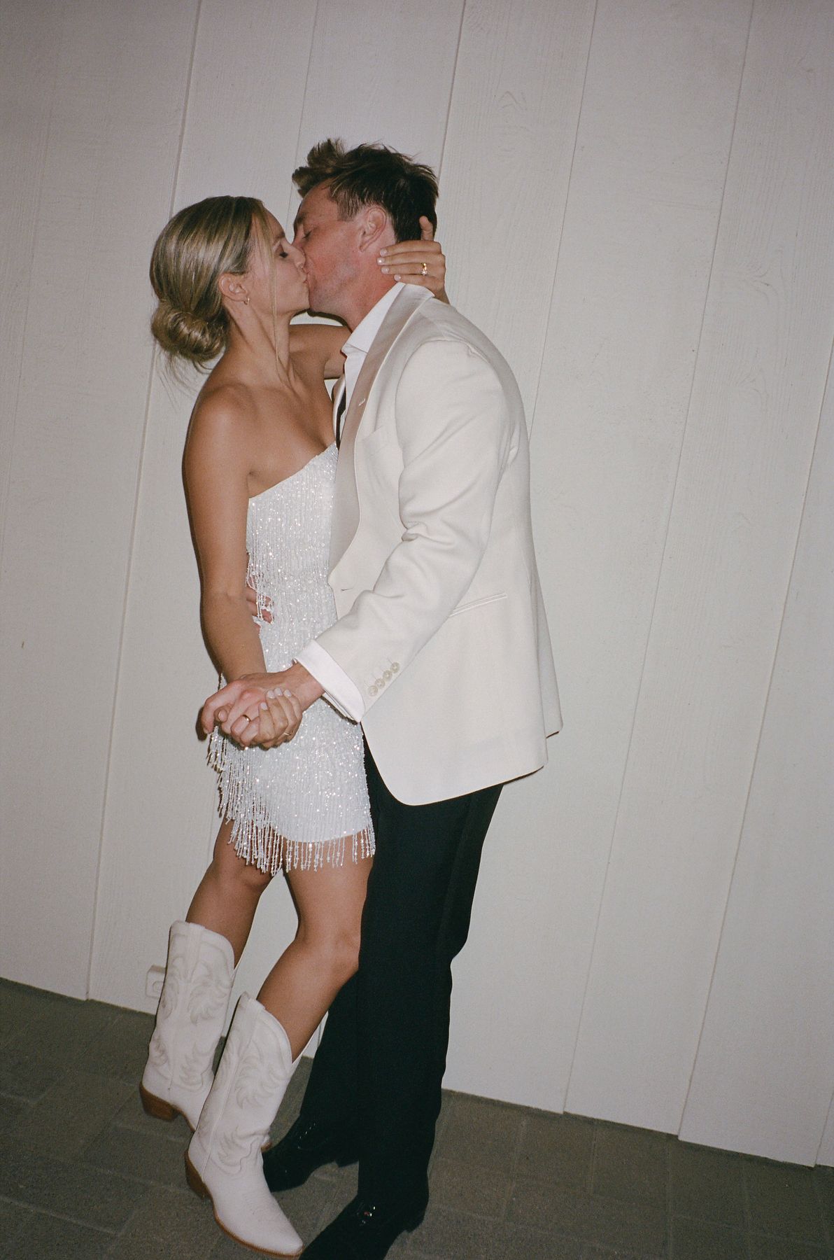 Couple in wedding attire sharing romantic dance moves in white room.