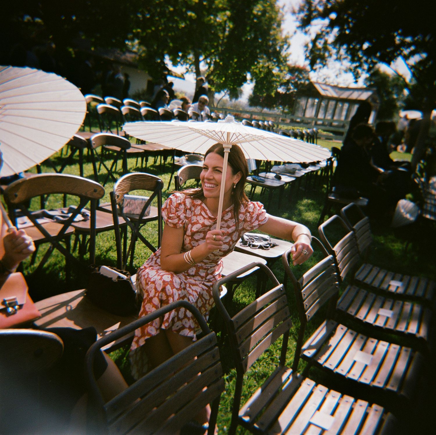 Wedding guests relax on wooden benches in an outdoor garden setting.