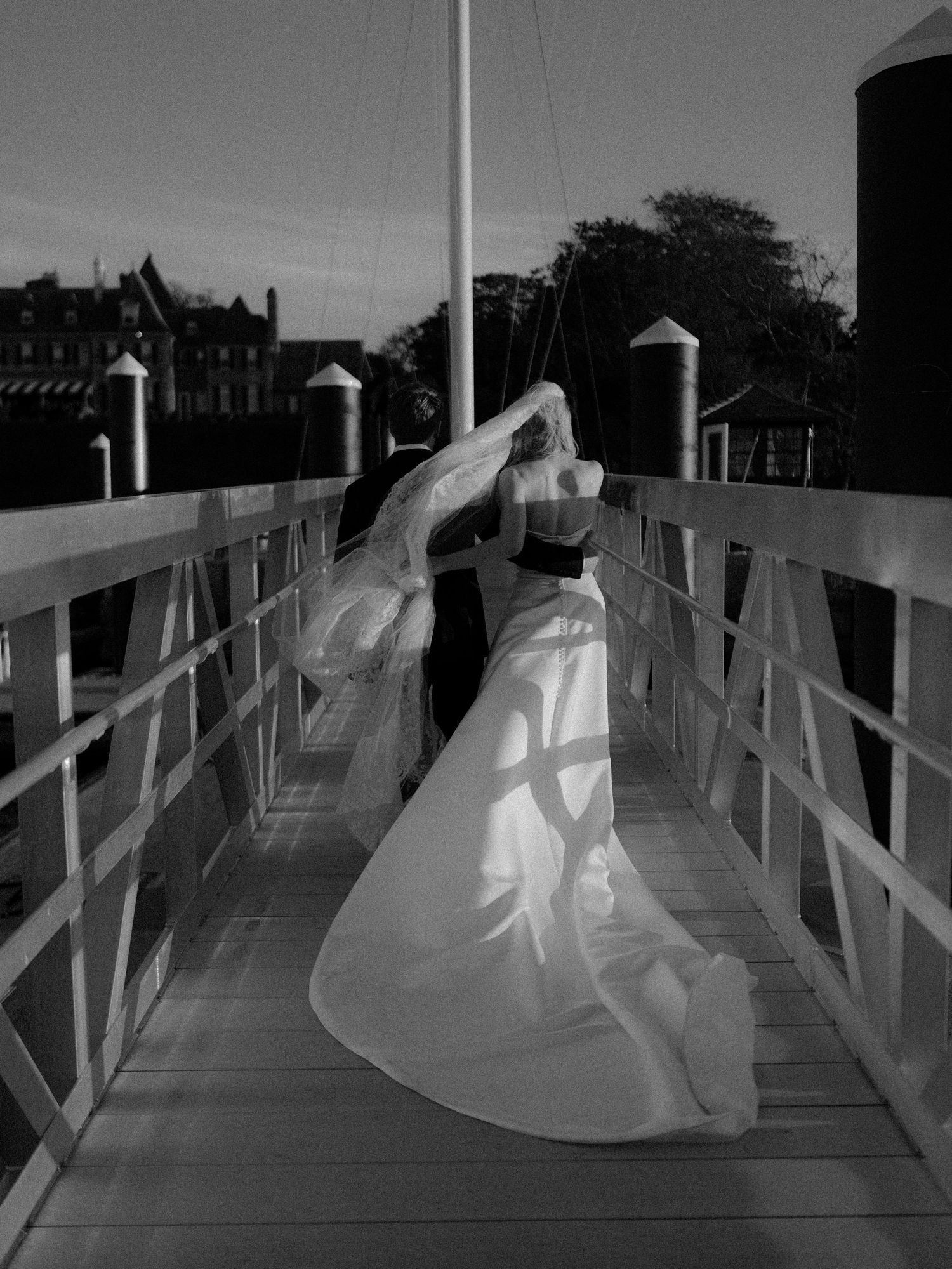 Black and white photo of a bride walking along a wooden boardwalk, her dress flowing in the wind.