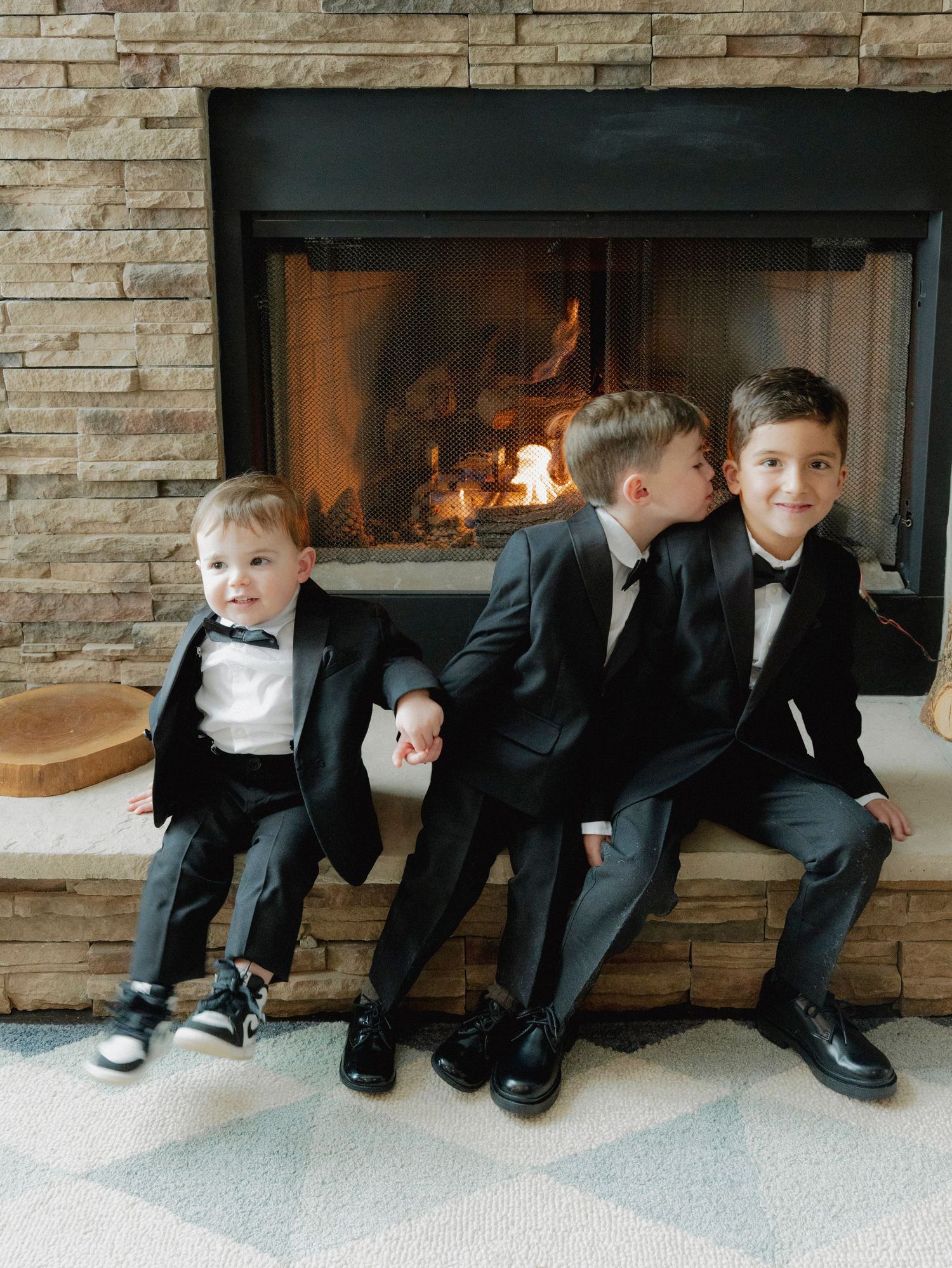 Young boys in formal suits sit in a row along a stone fireplace.