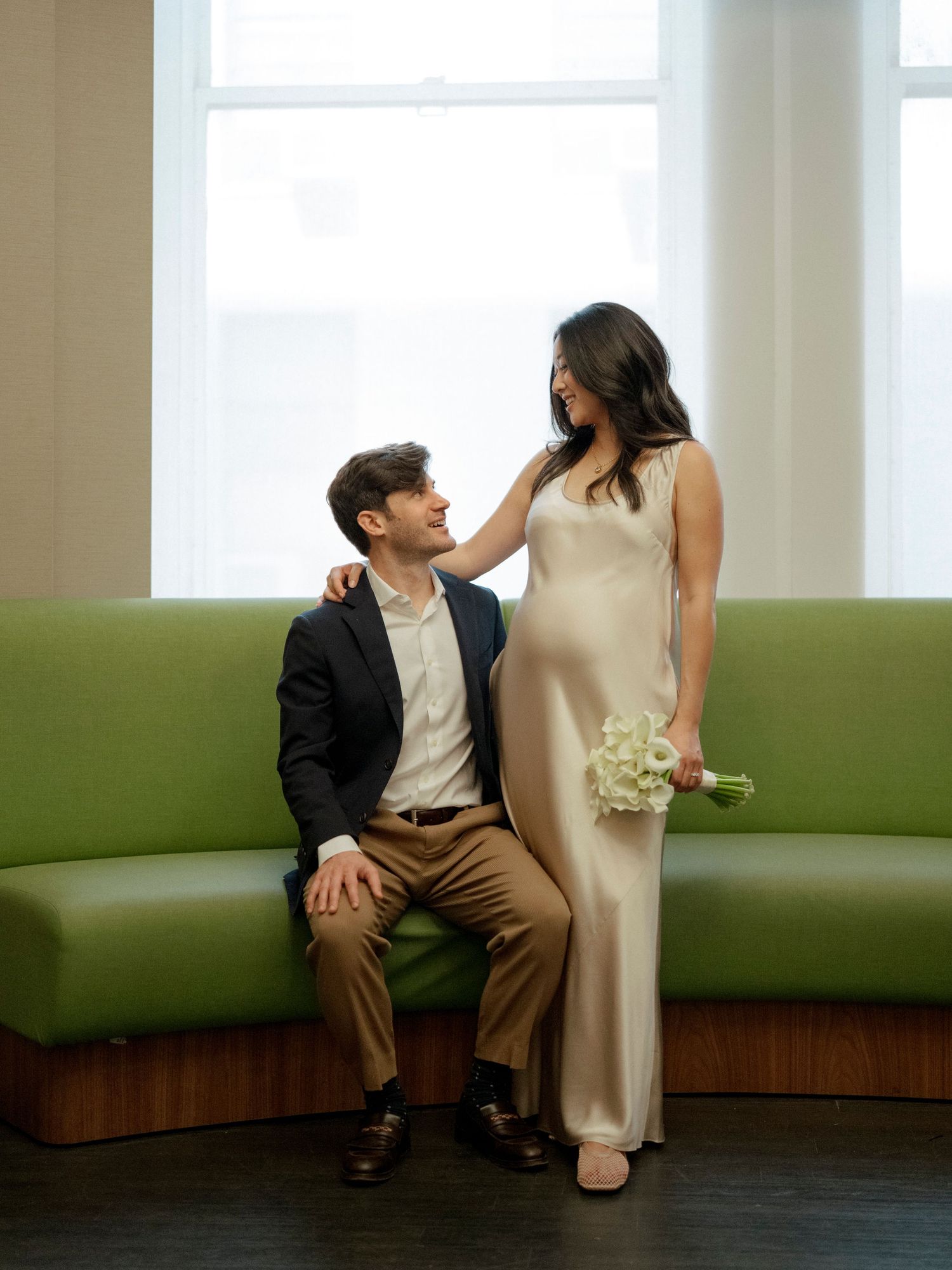Intimate moments captured on a curved green banquette seating area near bright windows.