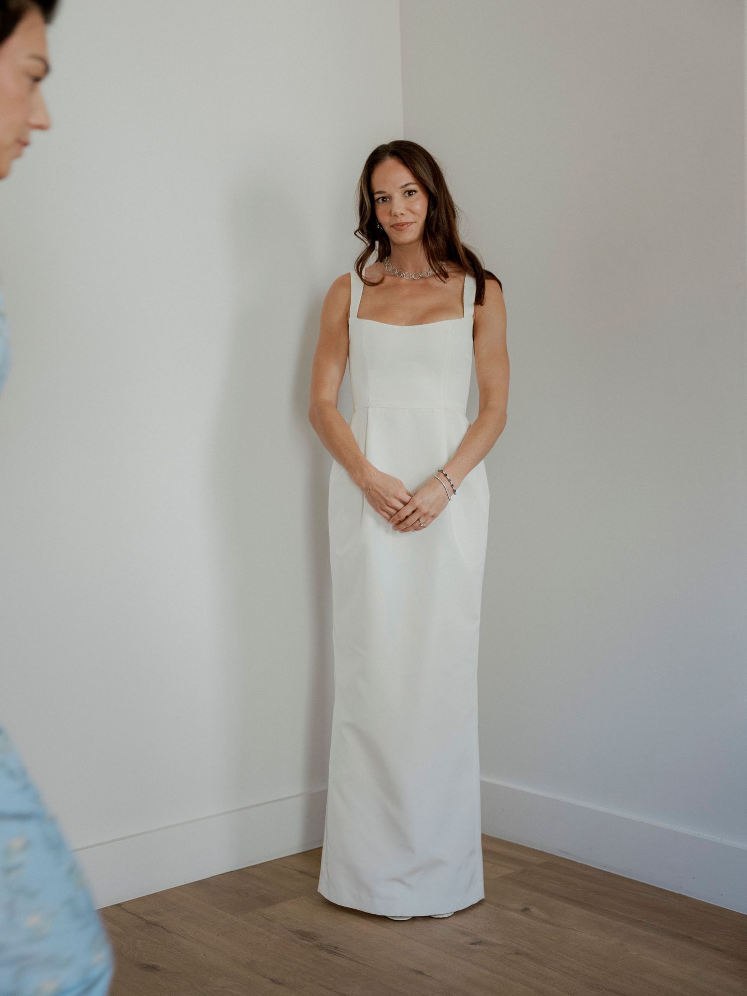 Elegant sleeveless white column wedding dress shown in a minimalist indoor setting.