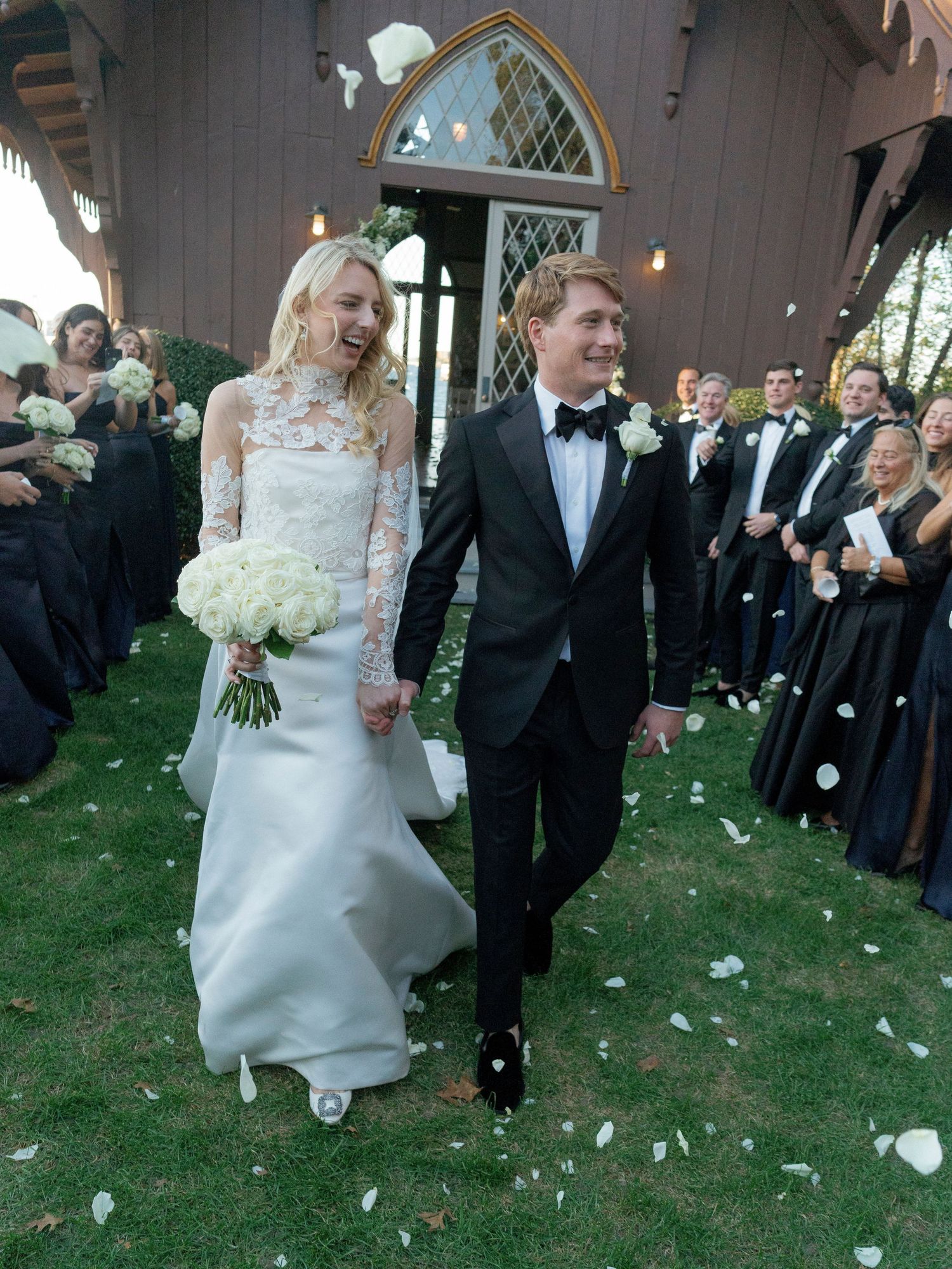 A bride and groom walk through a shower of white flower petals during their outdoor wedding celebration.