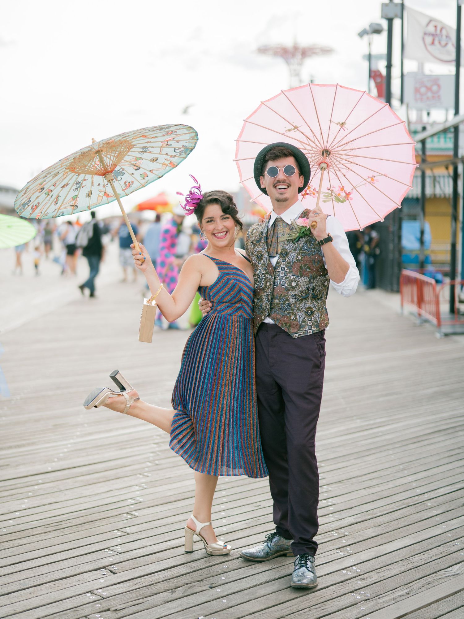 Vintage-styled couple dancing with parasols on a wooden boardwalk by the seaside.
