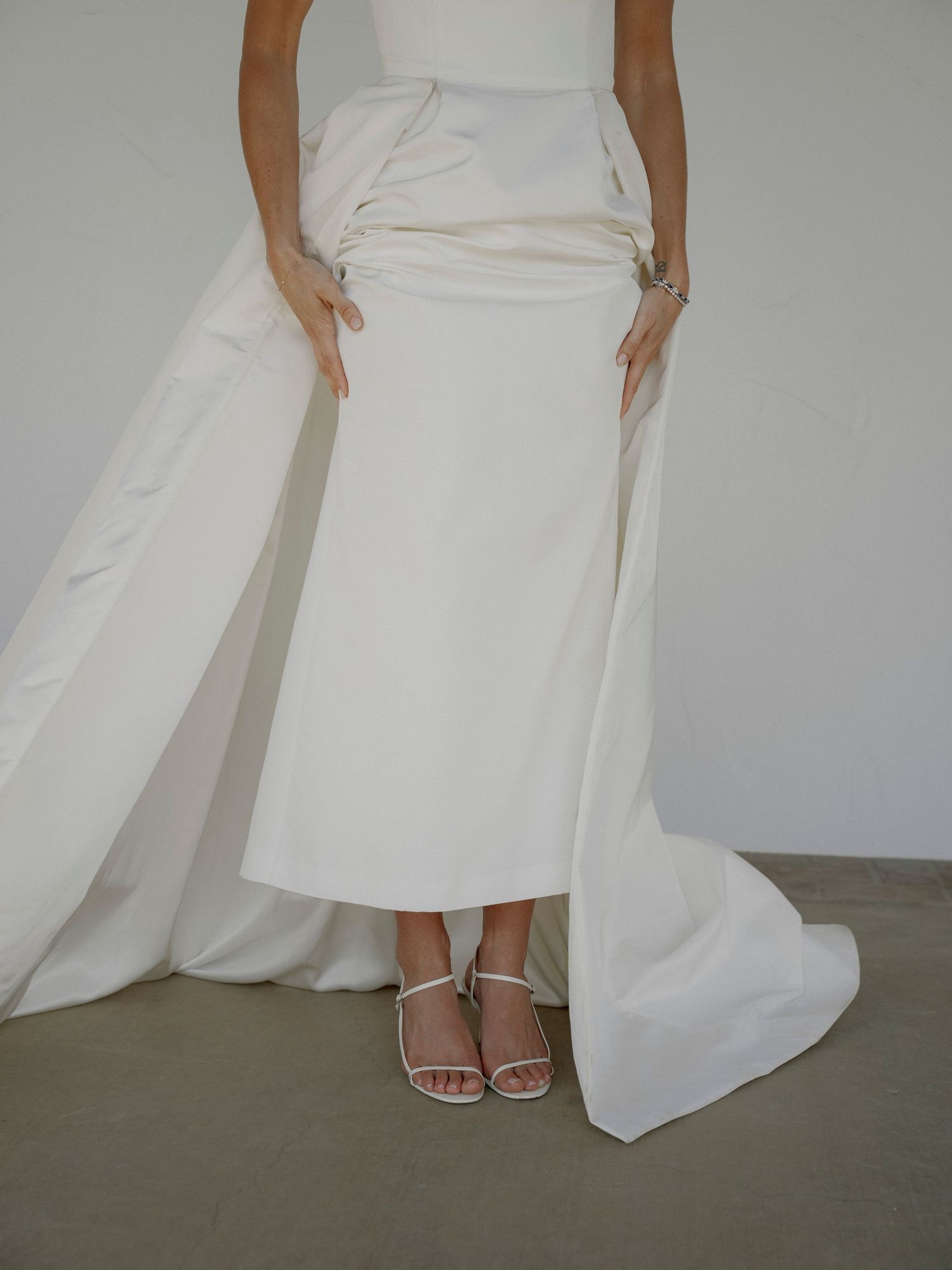 Close-up details of a white wedding dress and sandals against a light background.
