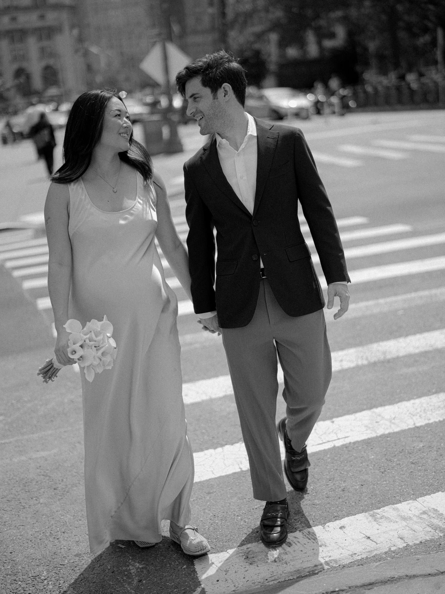A happy couple shares a laugh while crossing a city street in formal attire.