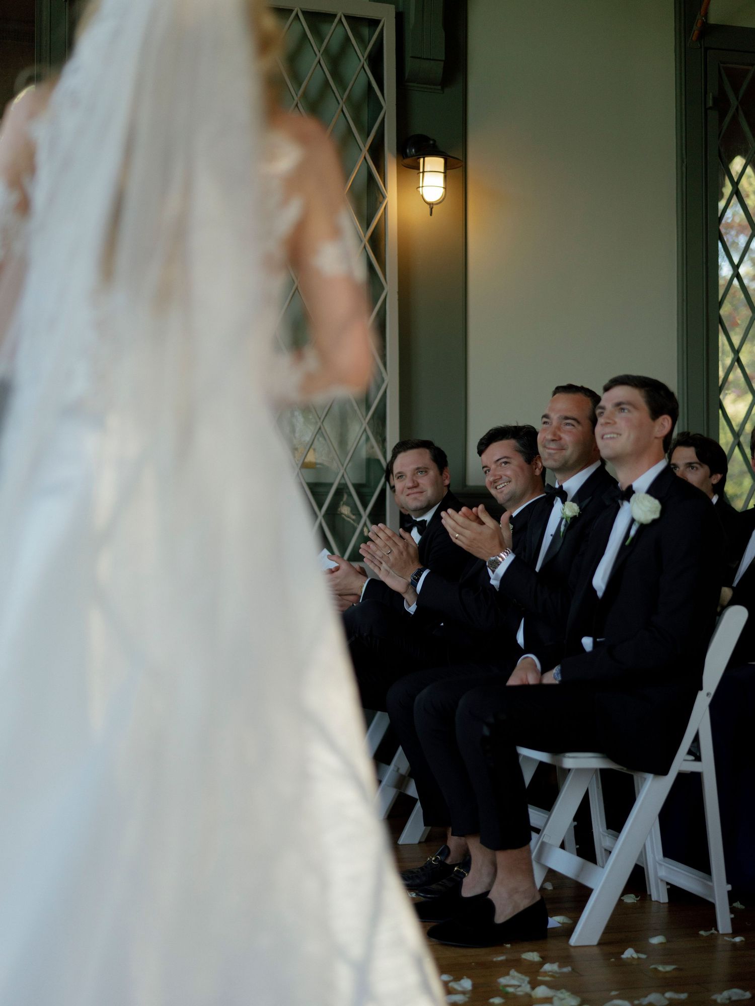 Wedding ceremony scene with guests in formal attire seated in white chairs watching the processional.