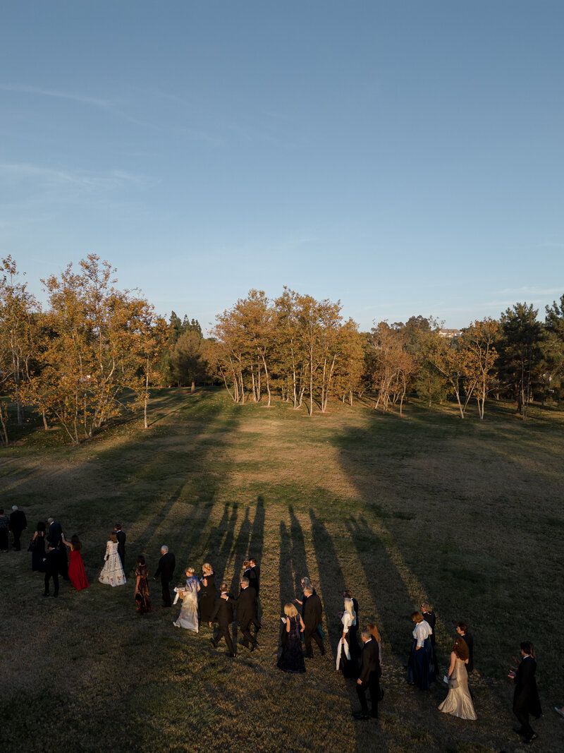 Wedding party lineup casting long shadows on grassy field during golden hour.