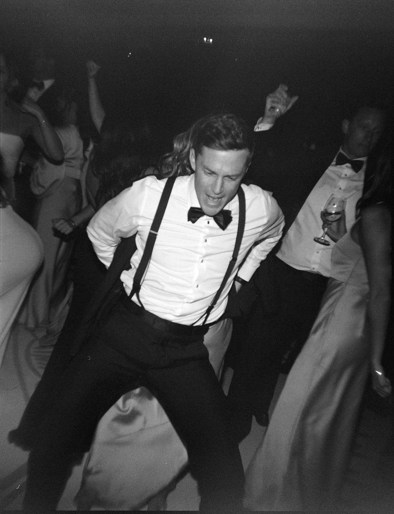 People dancing in formal attire at a dimly lit party or celebration.